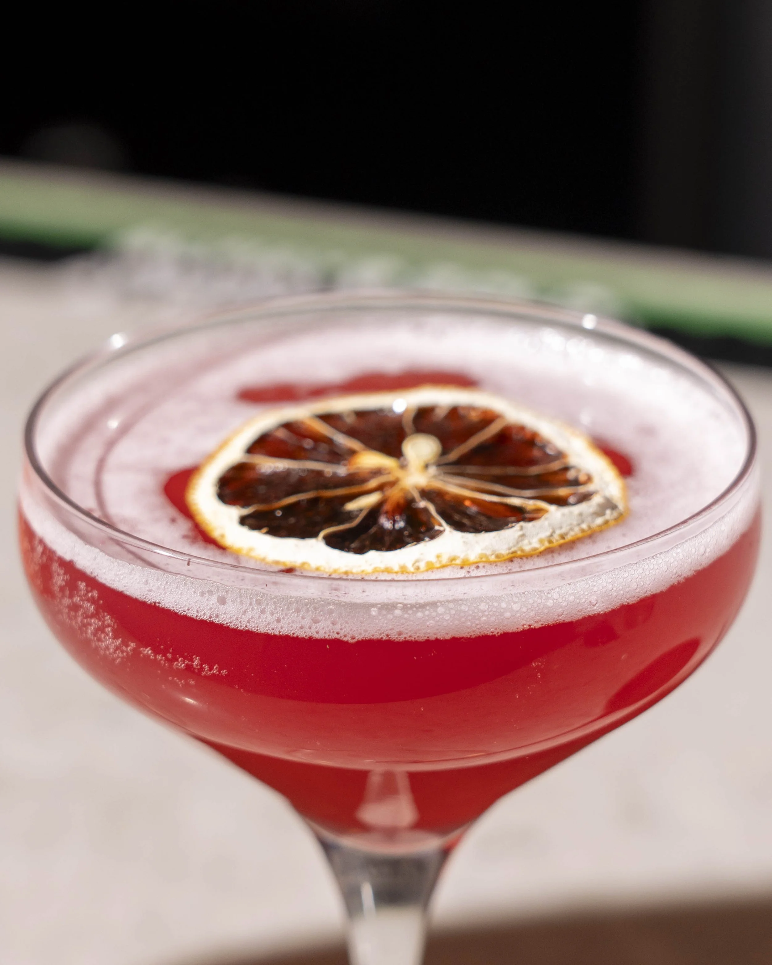 A cocktail drink in a coupe glass garnished with a slice of dried blood orange.