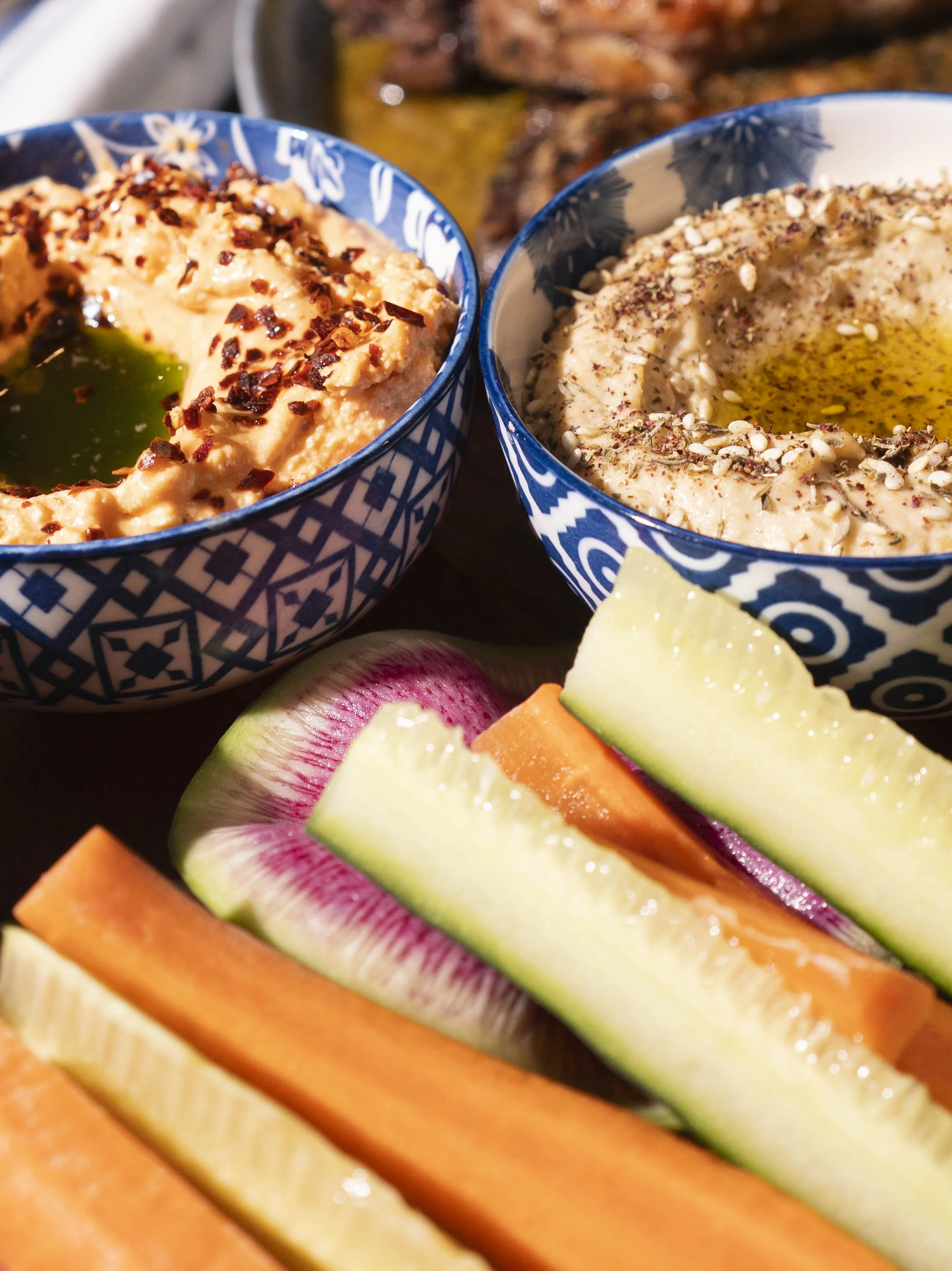 Two bowls of hummus with olive oil and spices, surrounded by slices of melon and cantaloupe.