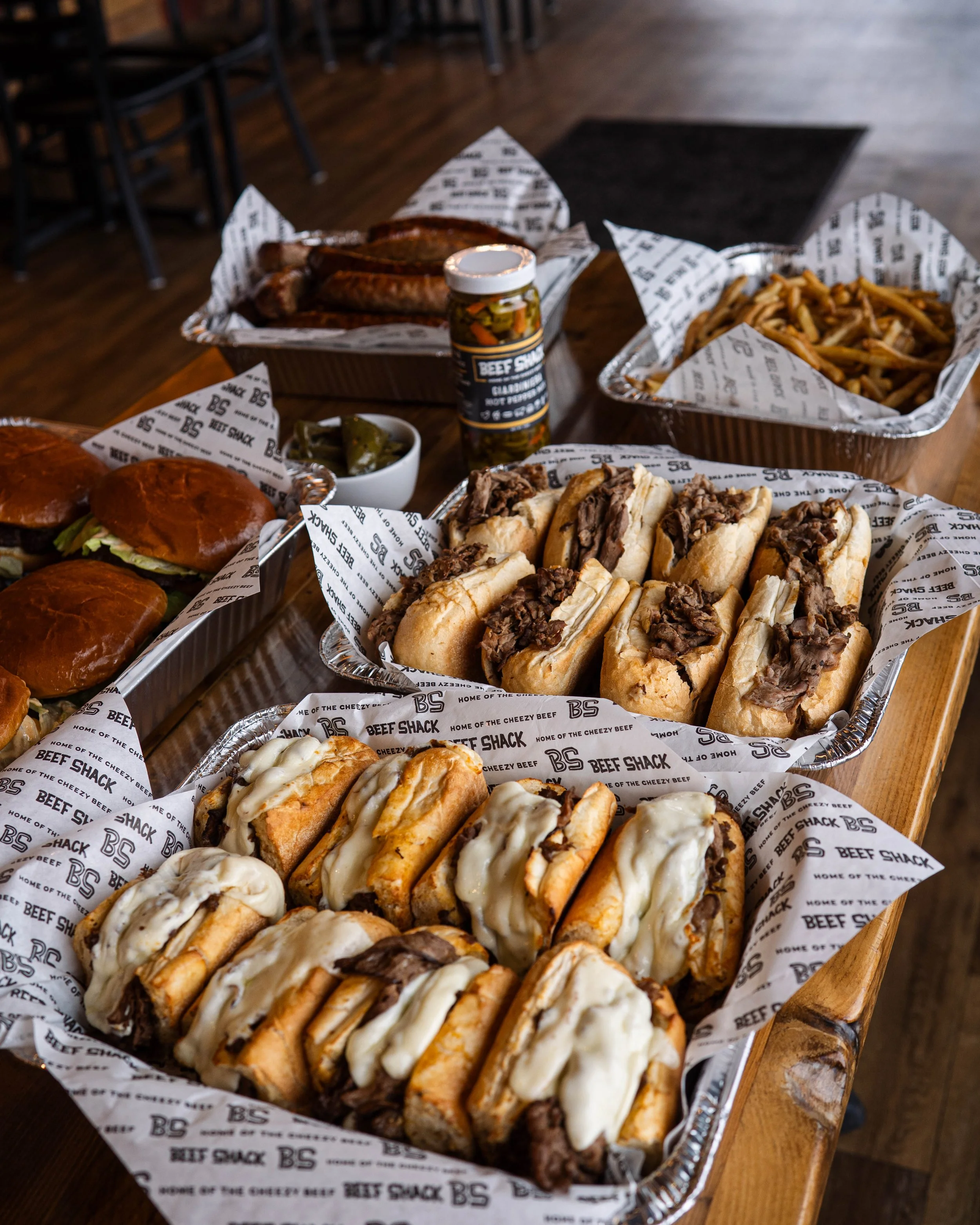 Assorted barbecue foods including sandwiches, hot dogs, ribs, fries, and pickles on a wooden table.