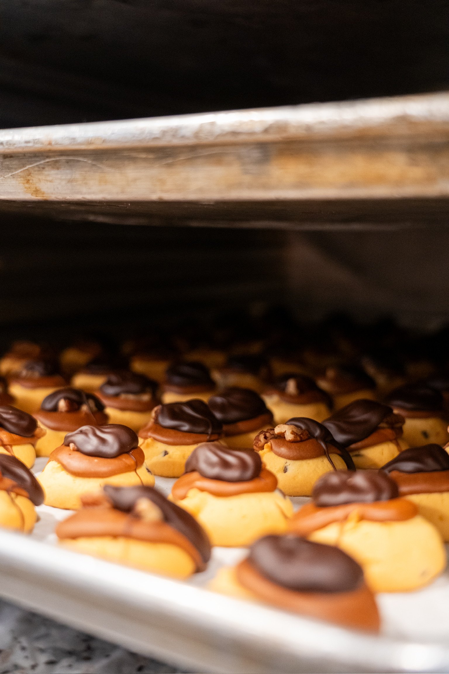 Cookies topped with chocolate and caramel cooling on a baking sheet in an oven.