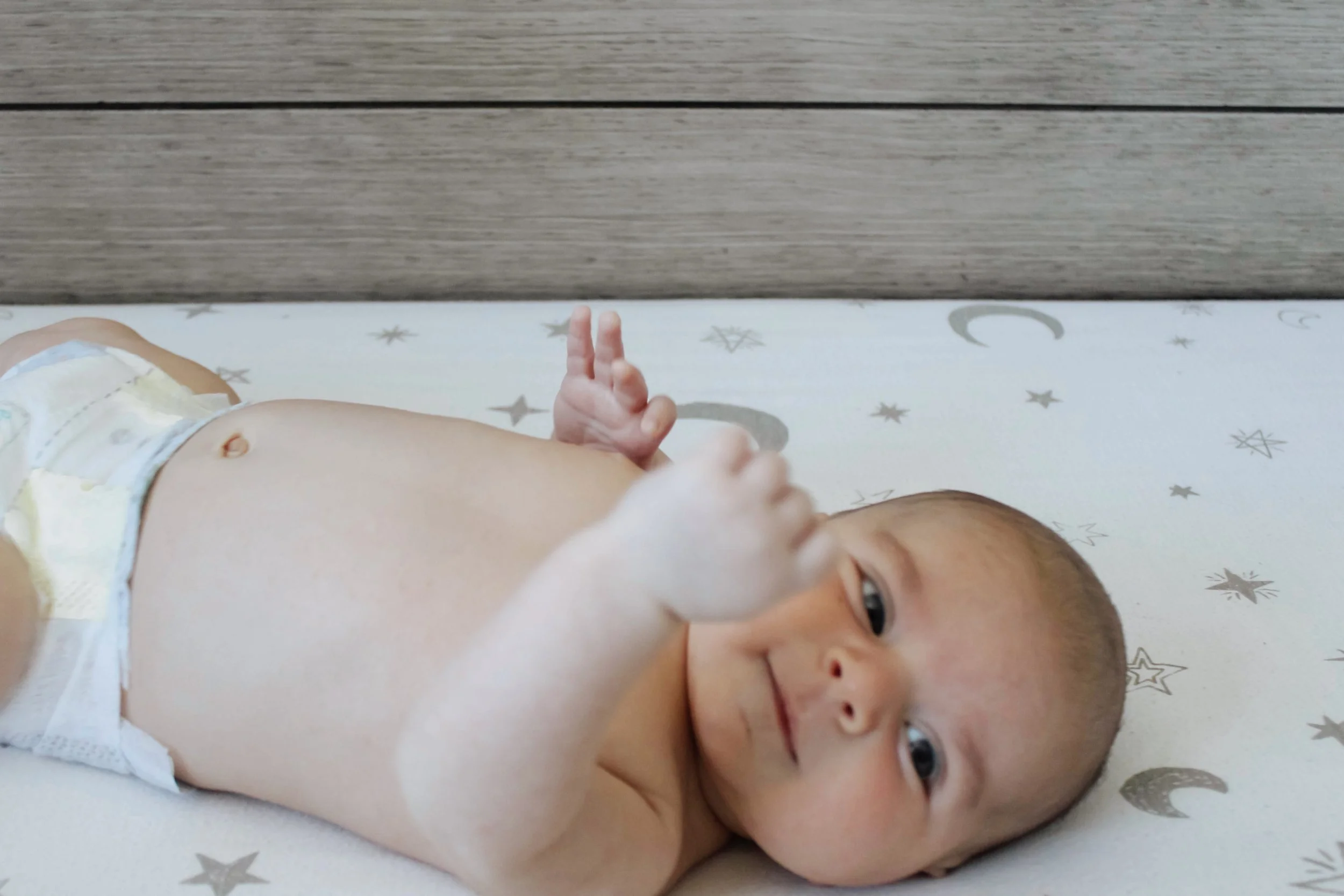 A baby lying on a star and moon printed changing pad, smiling and looking at the camera.
