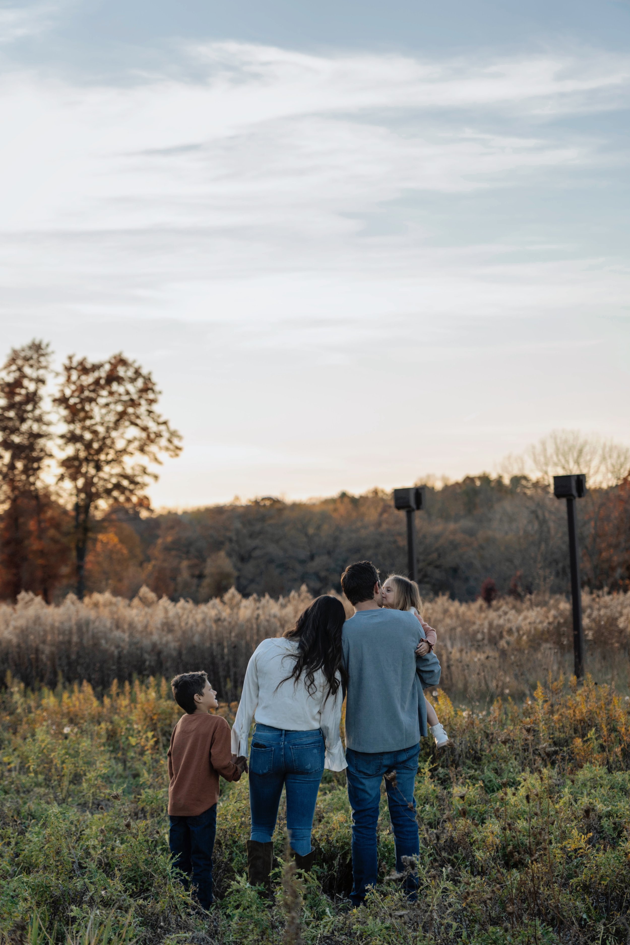 Family of four, including a man, woman, and two children, enjoying a walk outdoors in a park during autumn sunset