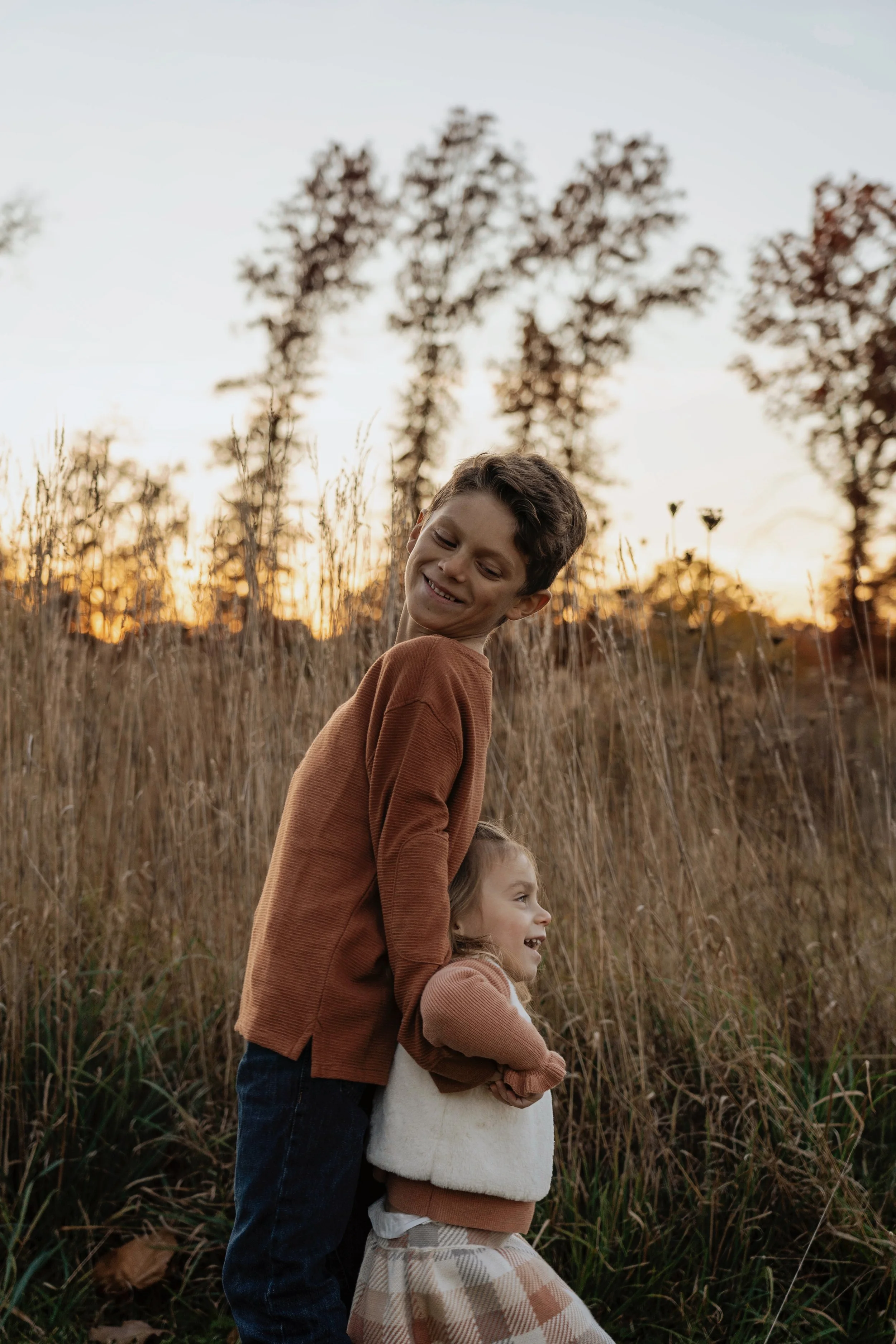 A young boy and girl playing together in a field of tall grass during sunset, smiling and having fun.