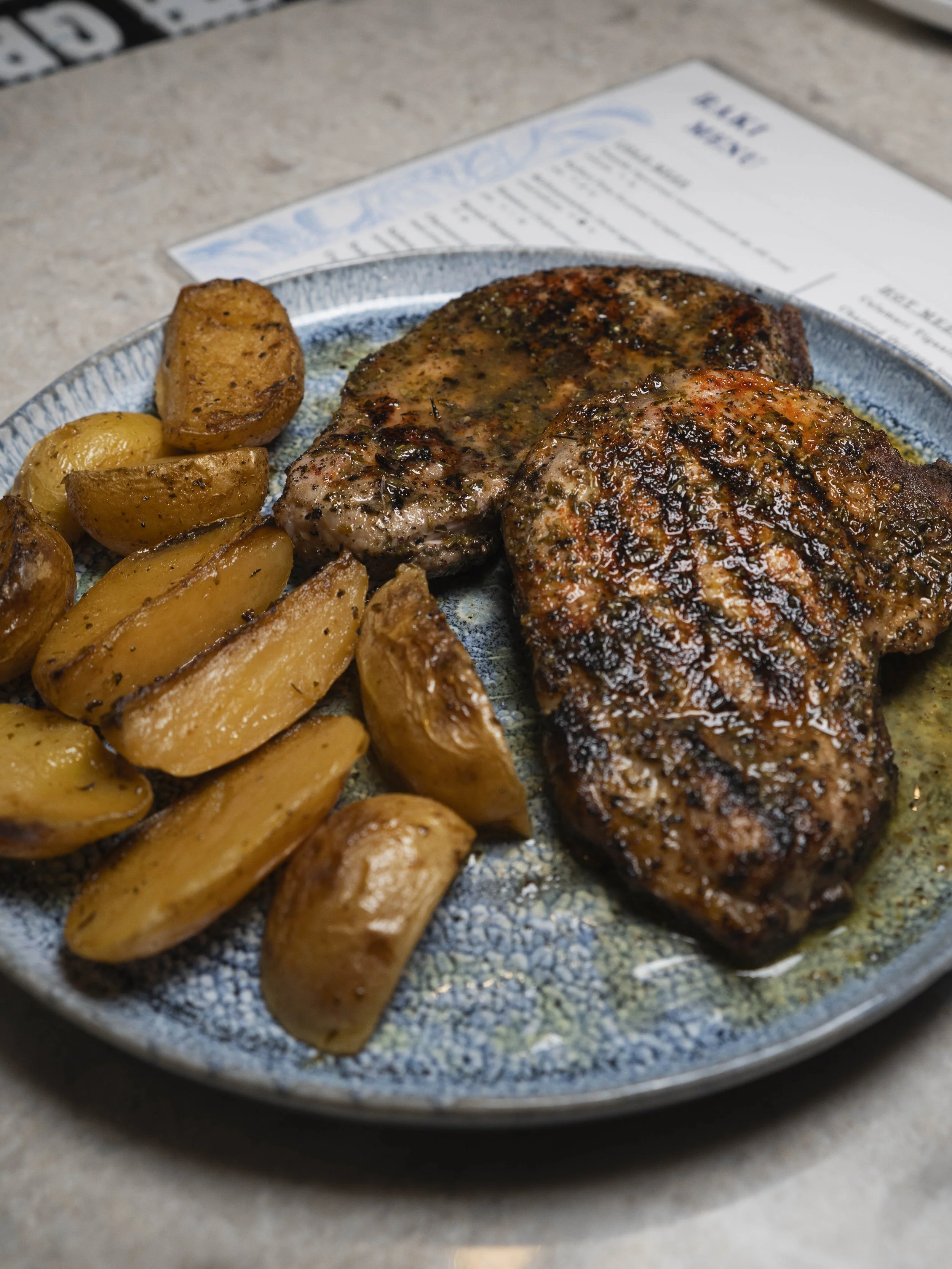 A plate of grilled steaks with roasted potatoes on a restaurant table.