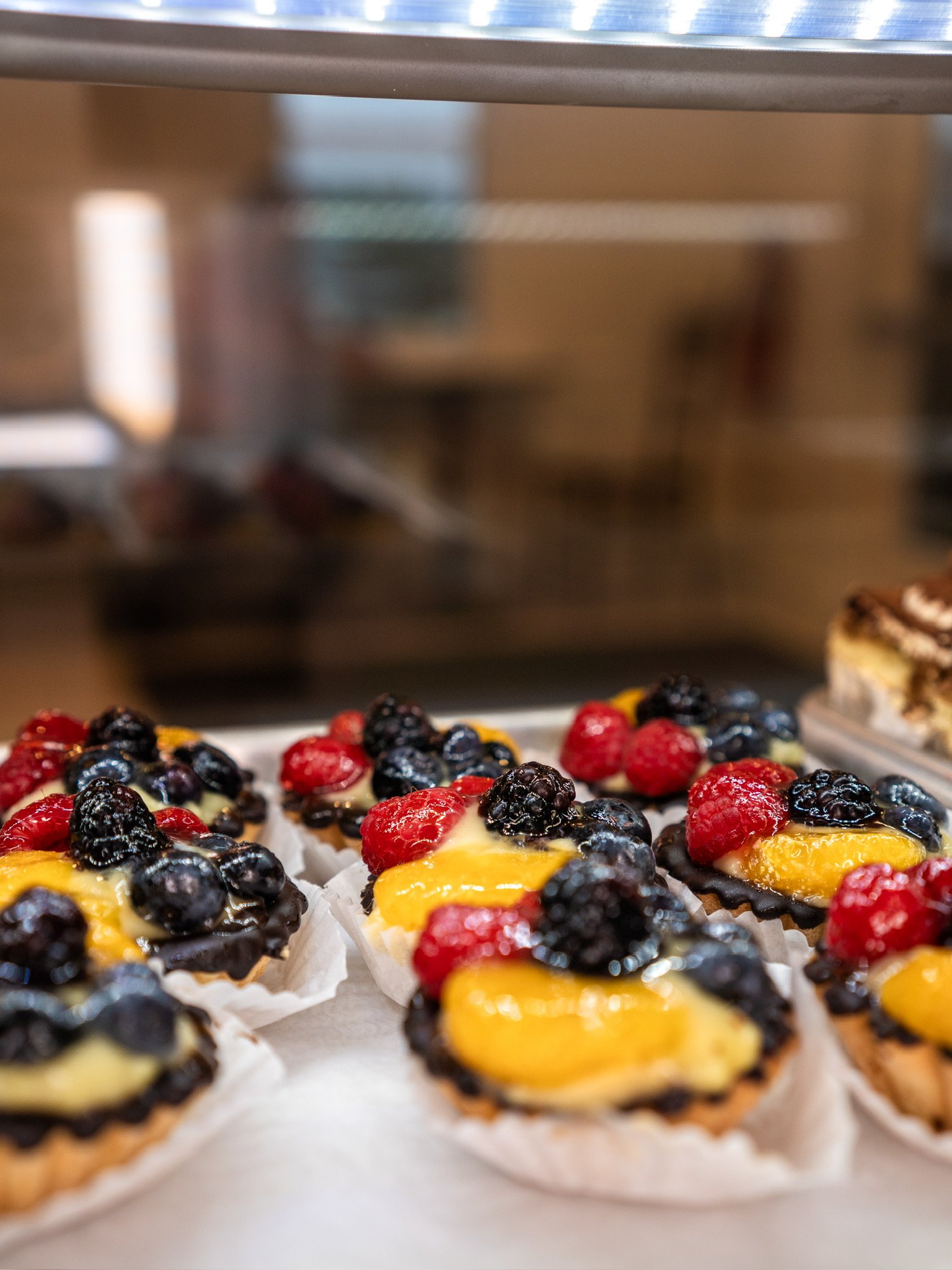 Assorted fruit tarts topped with blackberries, raspberries, and a yellow glaze, arranged on a tray.