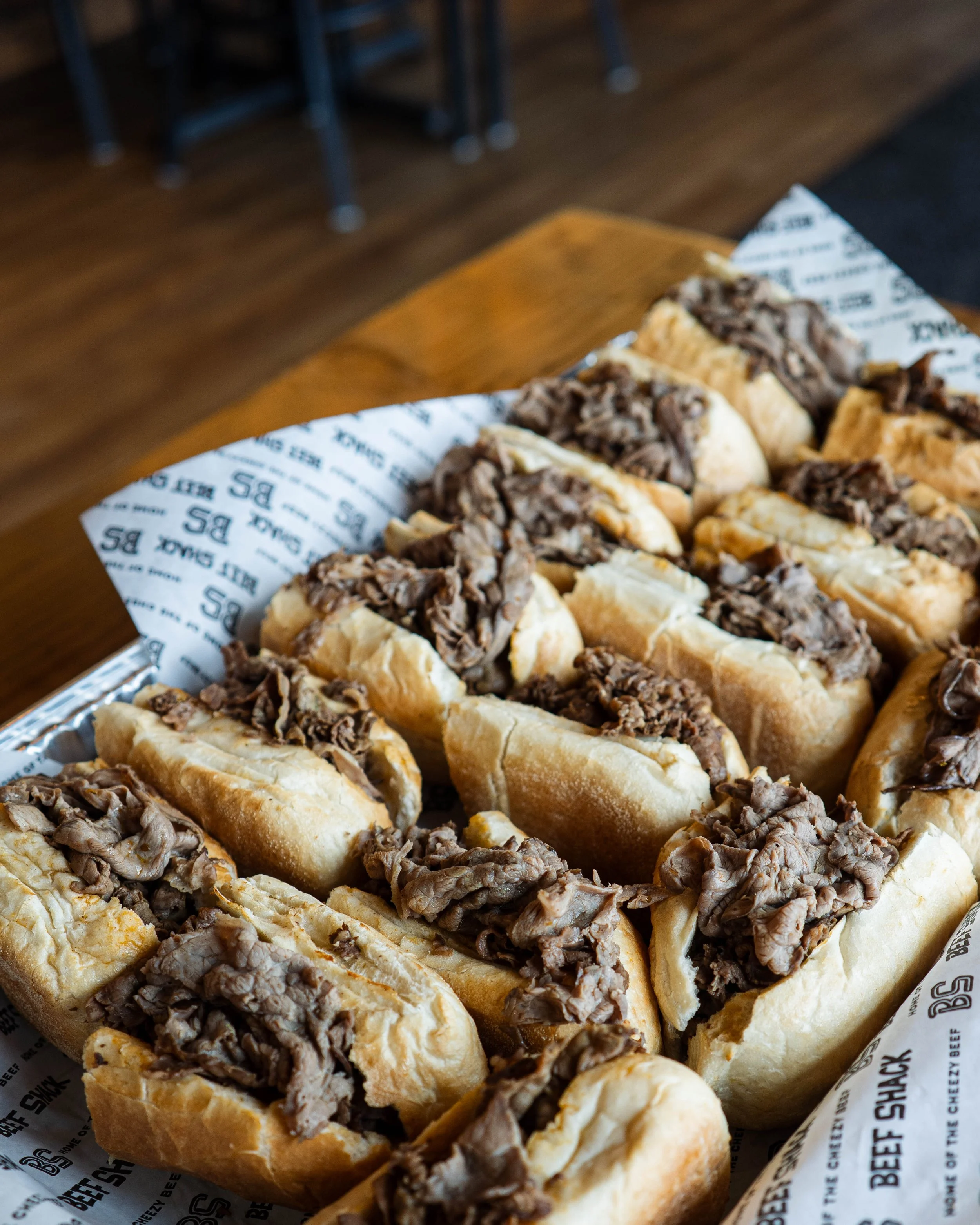 Beef sandwiches with shredded beef on toasted hoagie rolls in a basket lined with branded paper