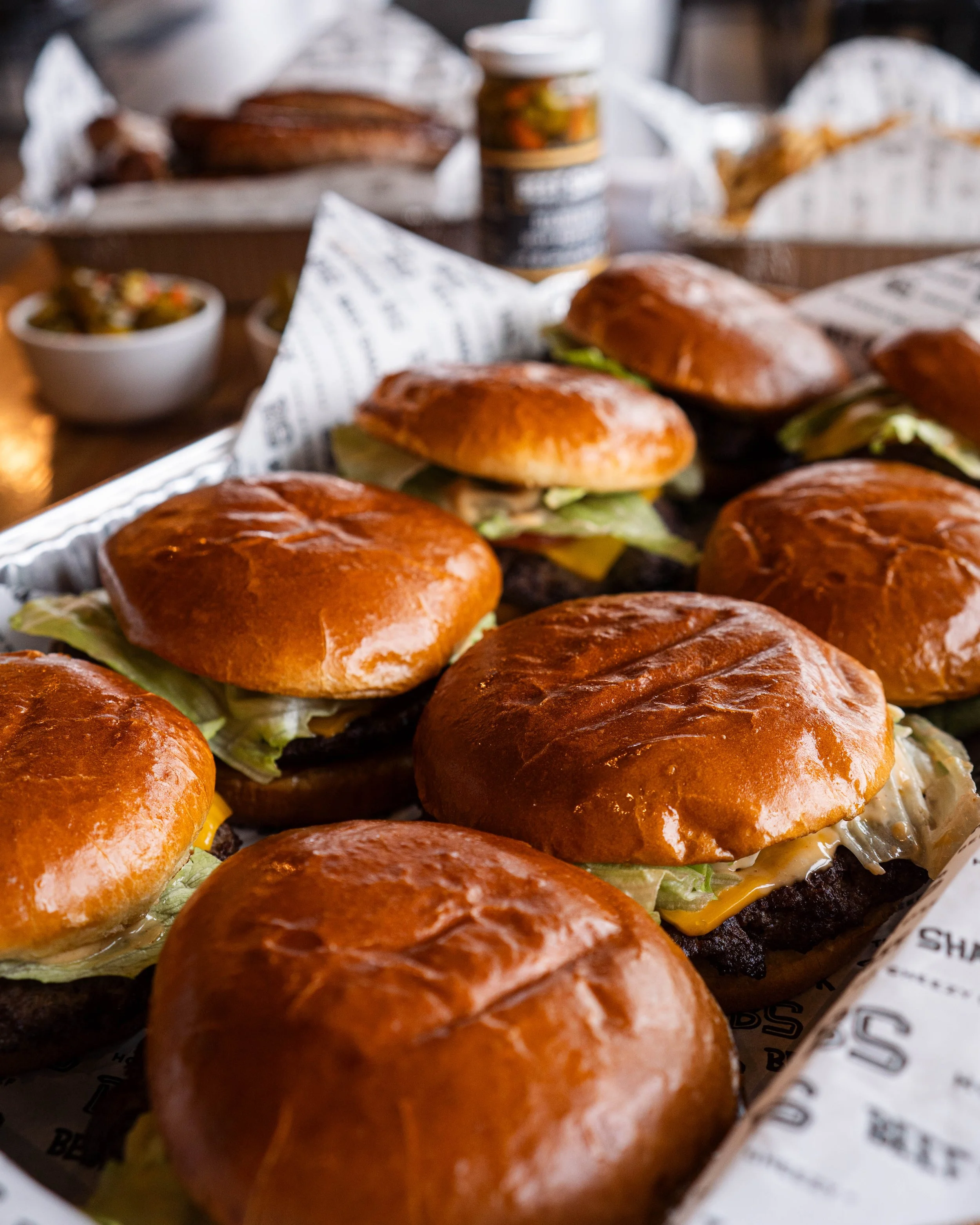 Close-up of a tray of cheeseburgers with lettuce and pickles, in a casual dining setting.