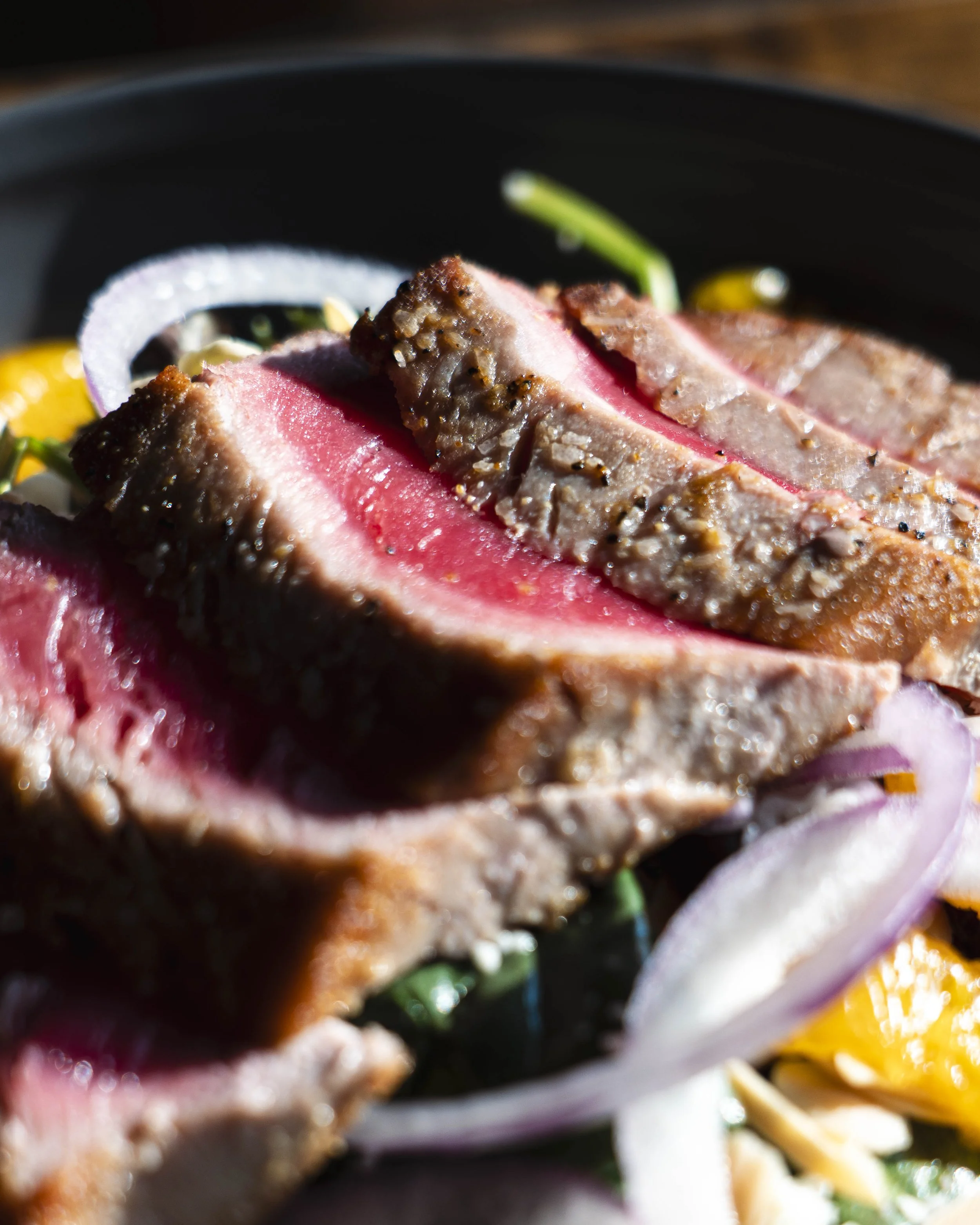 Close-up of sliced medium-rare steak with a pink center, served with sliced red onions and other vegetables.