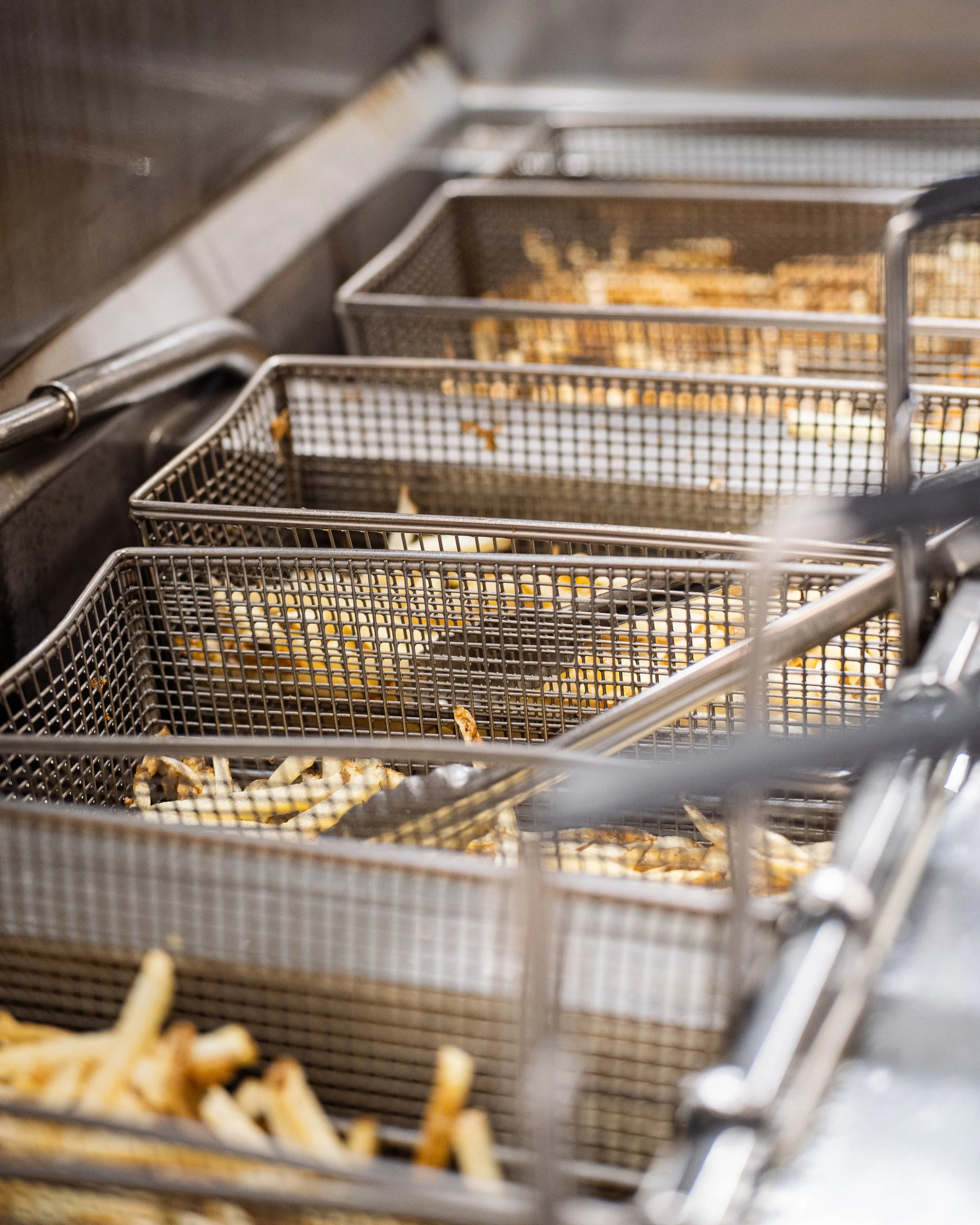 Empty metal fry baskets in a deep fryer with some fried food remnants inside.
