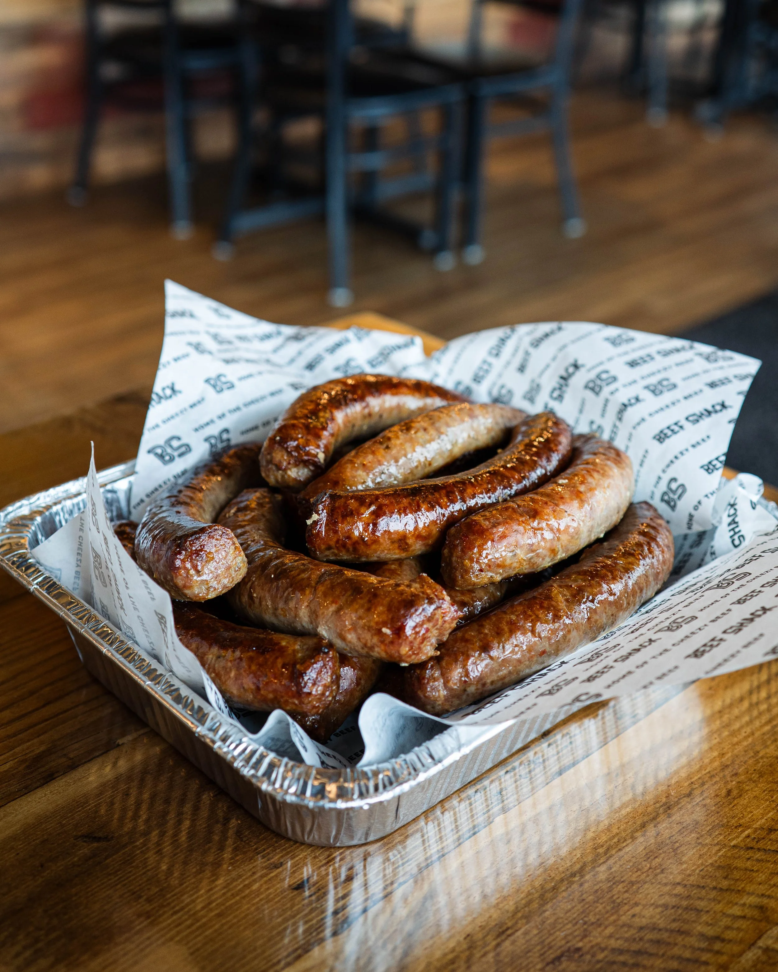 A tray of cooked sausages on paper lining, placed on a wooden table in a restaurant.