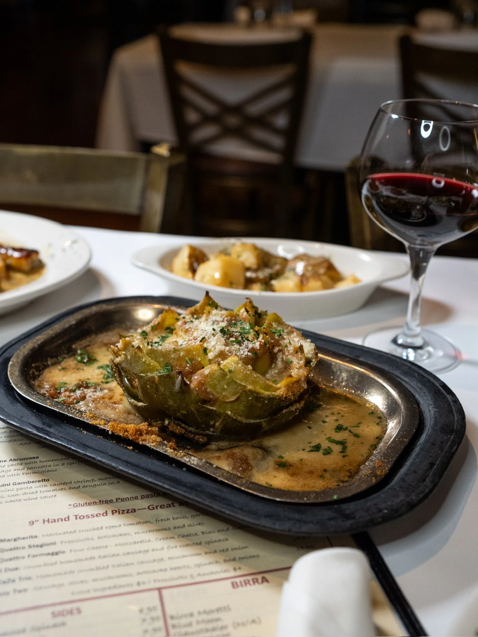 A seafood dish served in a carved-out vegetable shell on a black platter, with a glass of red wine and additional dishes in the background on a restaurant table.