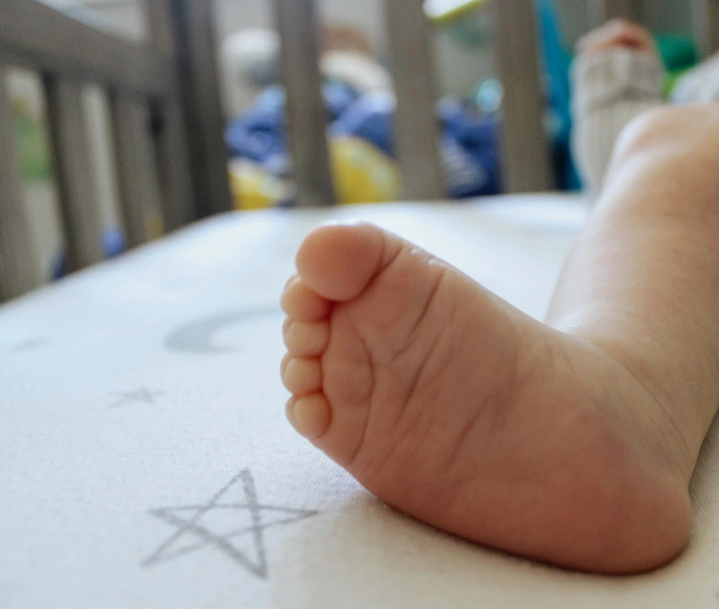 Close-up of a baby's hand resting on a white surface with a hand-drawn star. Blurred background showing part of a railing and indistinct objects.
