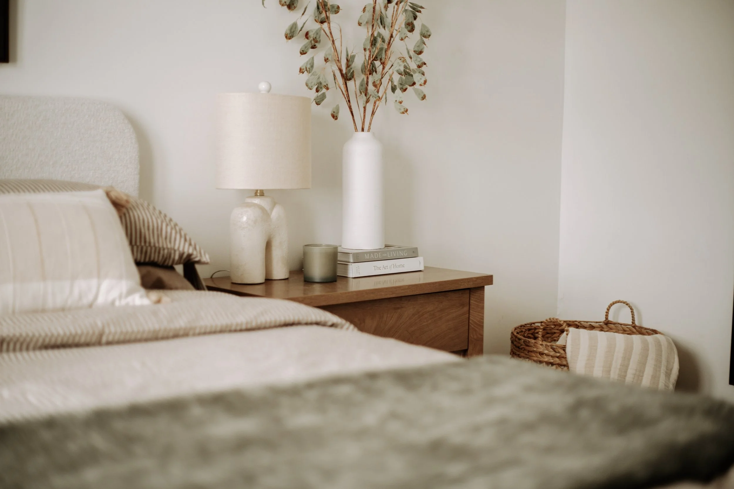 Layered bedroom design with striped bedding, warm wood nightstand and neutral textiles in Delano, Minnesota.