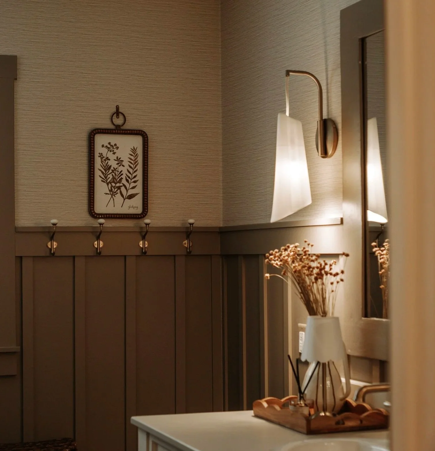 Twin Cities bathroom renovation with dark wainscoting, textured grasscloth wallpaper, brass wall sconce and vintage-inspired details.