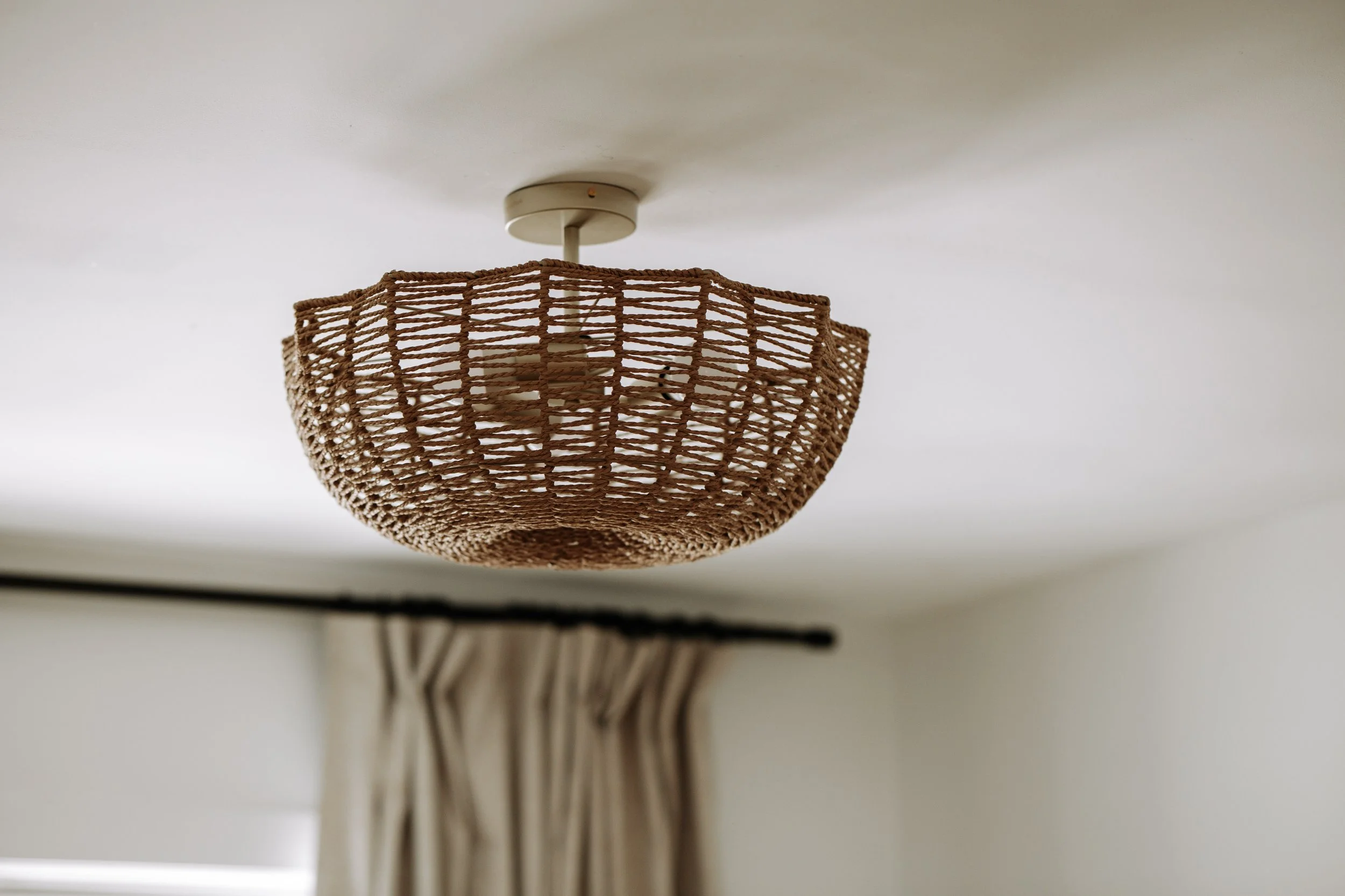 Layered neutral bedroom with upholstered headboard, floral artwork and woven pendant light.