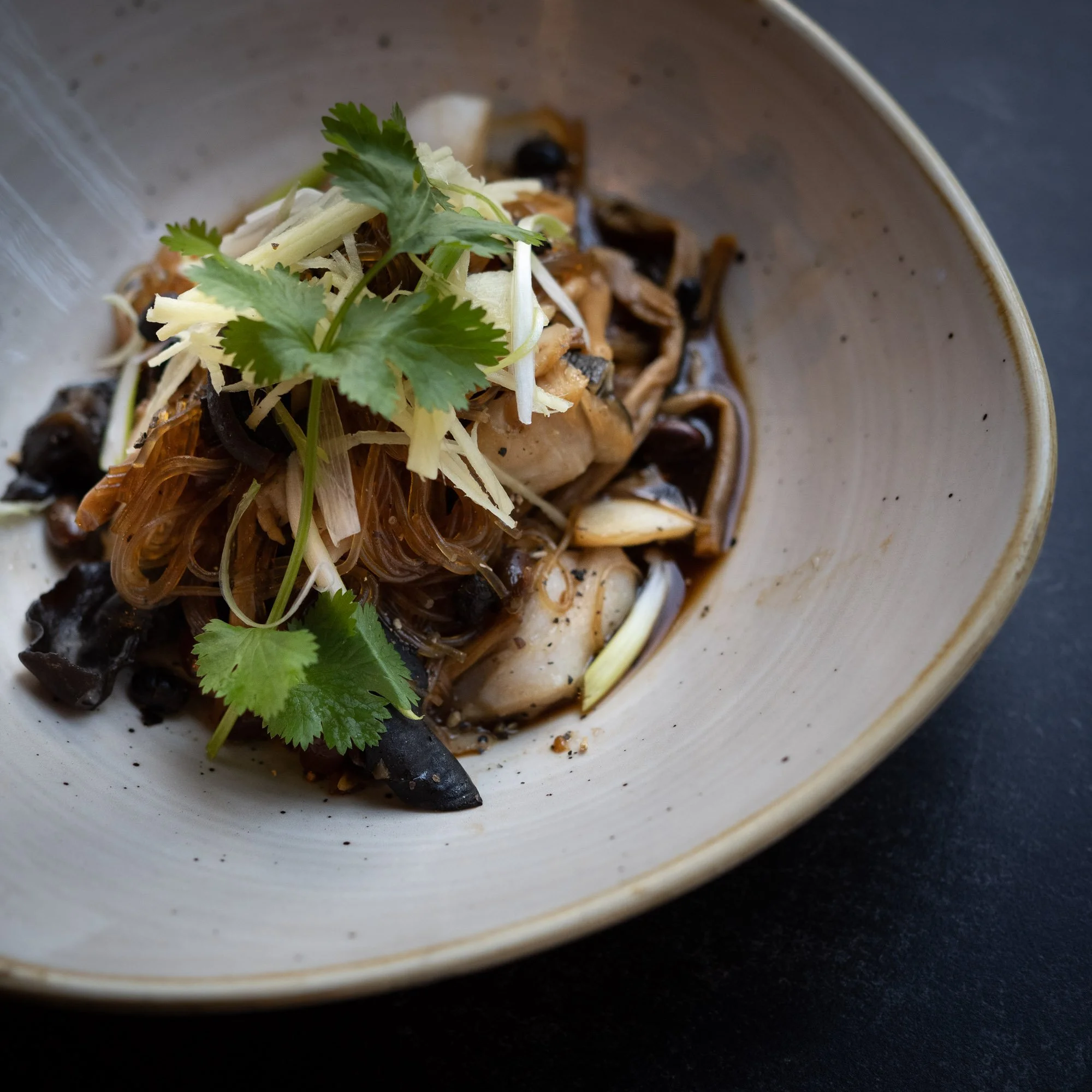 A bowl of Asian-inspired noodles with vegetables and herbs, garnished with cilantro.