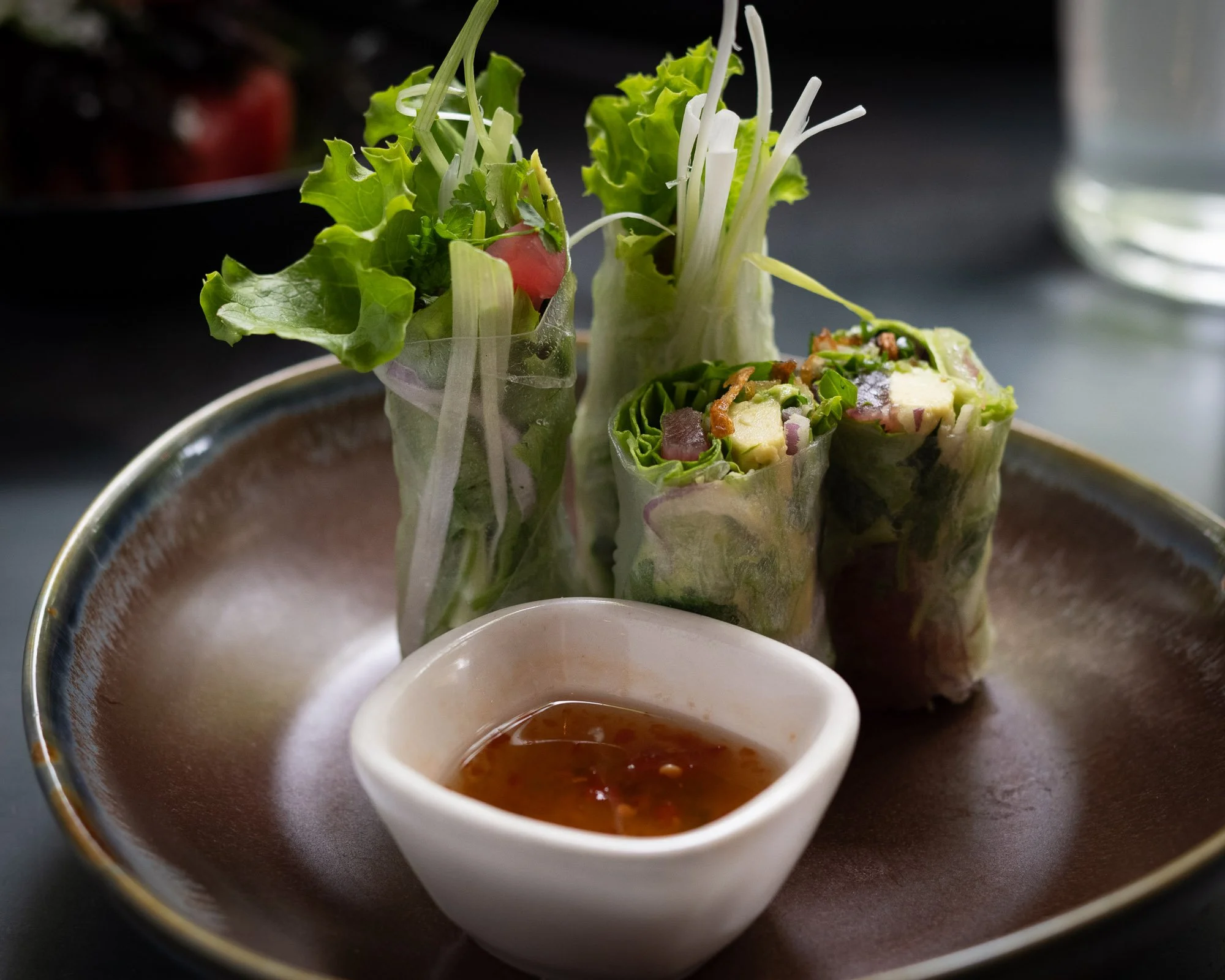Three Vietnamese spring rolls with fresh vegetables and herbs, served with a small dish of dipping sauce.