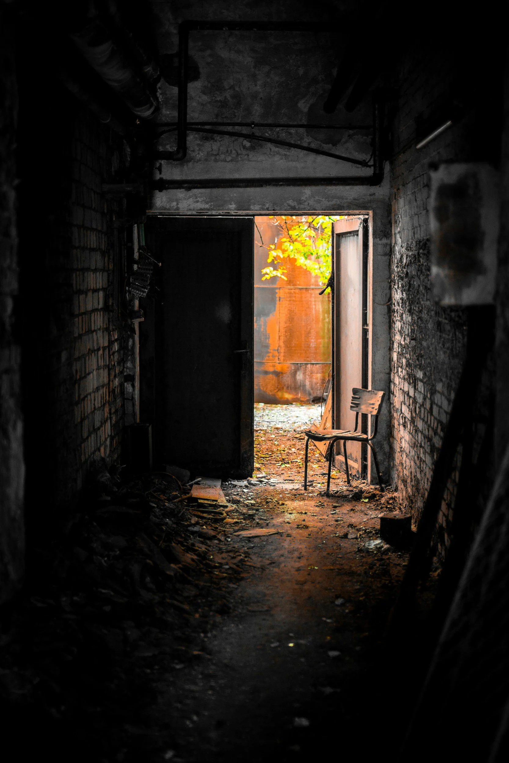 Open door with a chair holding it that leads into a light-filled courtyard from a dark hallway