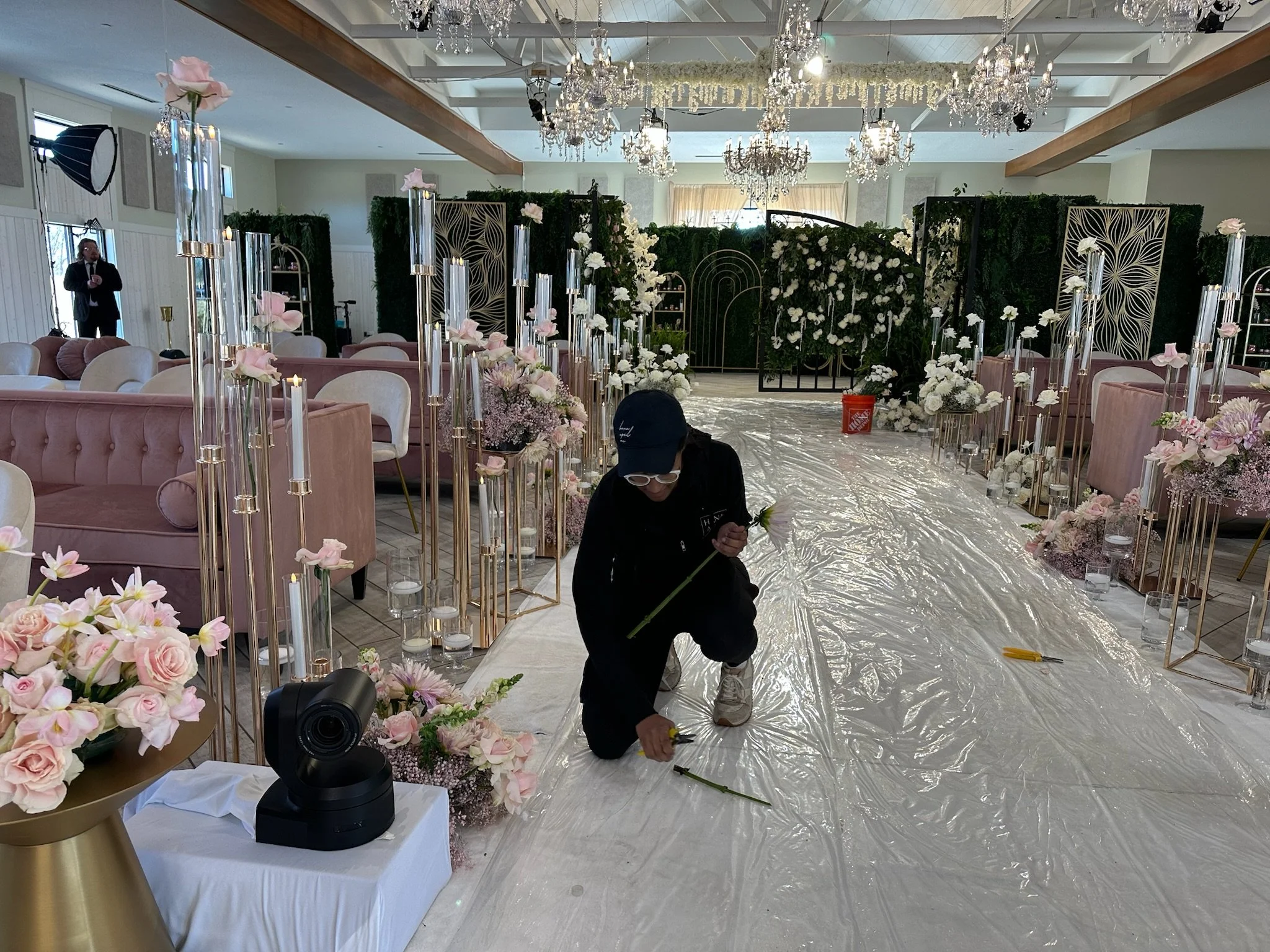 Alexandra Moss setting up floral decorations for a Ben and Sara's Netflix Love is Blind wedding ceremony inside Equestria West with pink and white flowers, candles, and elegant chandeliers.