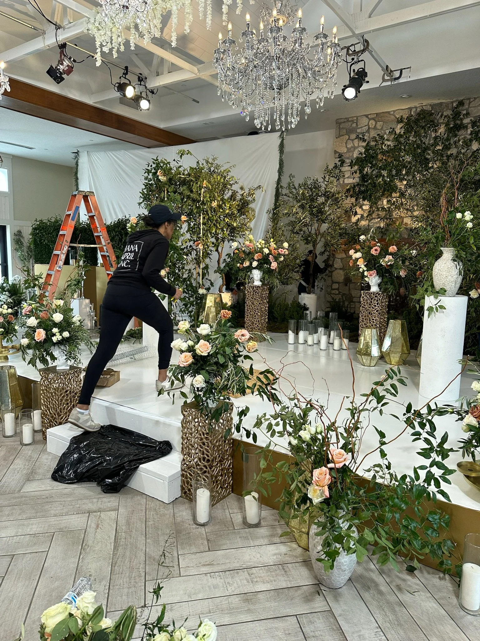 Interior of Equestria West in Chaska, MN setup for Monica and Joey's Wedding from Netflix Love is Blind with flowers, vases, candles, and a large chandelier, with a woman arranging decorations.