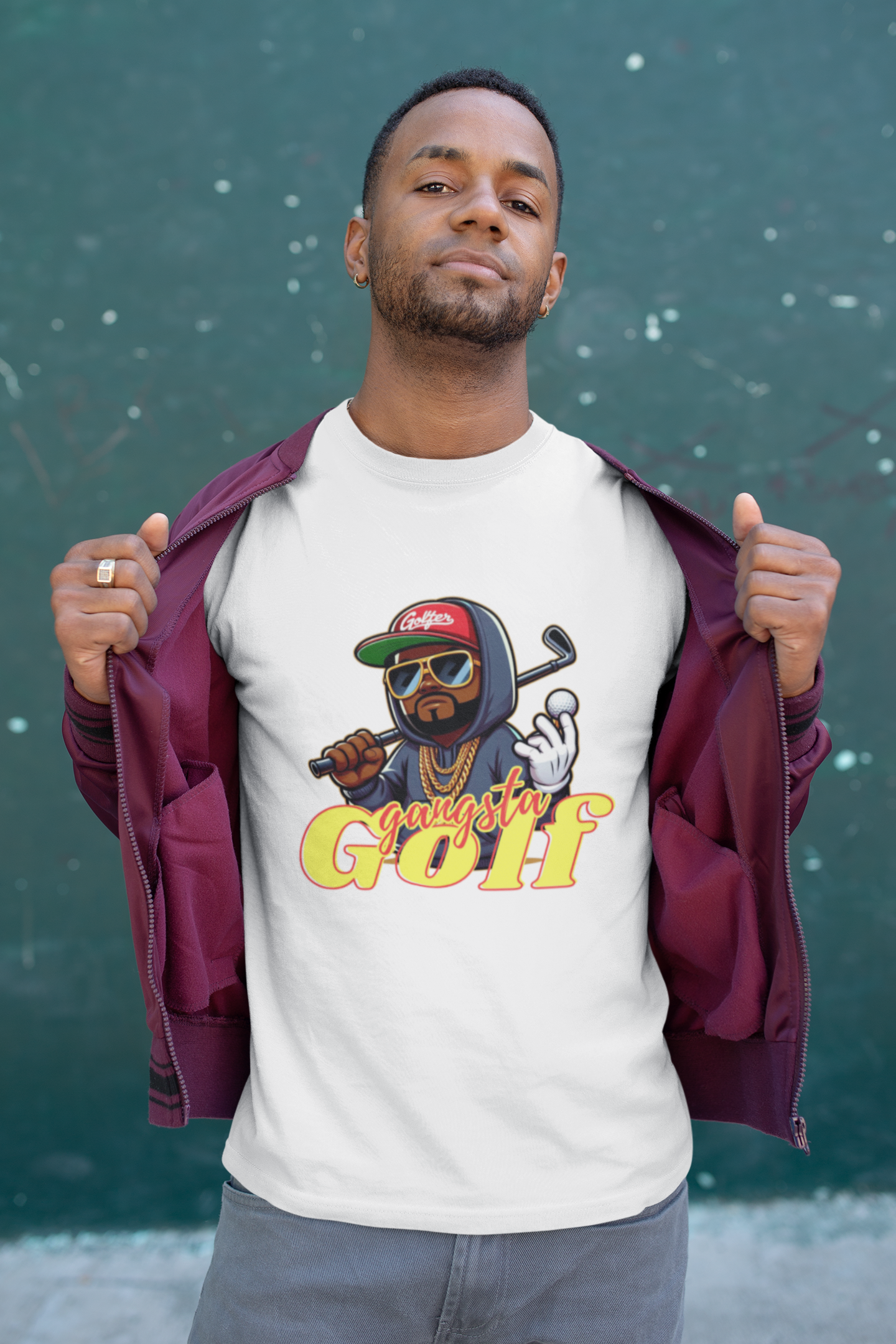 Person wearing a white 'Gangsta Golf' t-shirt with a cartoon character holding a golf club and ball, dressed in a burgundy jacket, standing against a green speckled background.