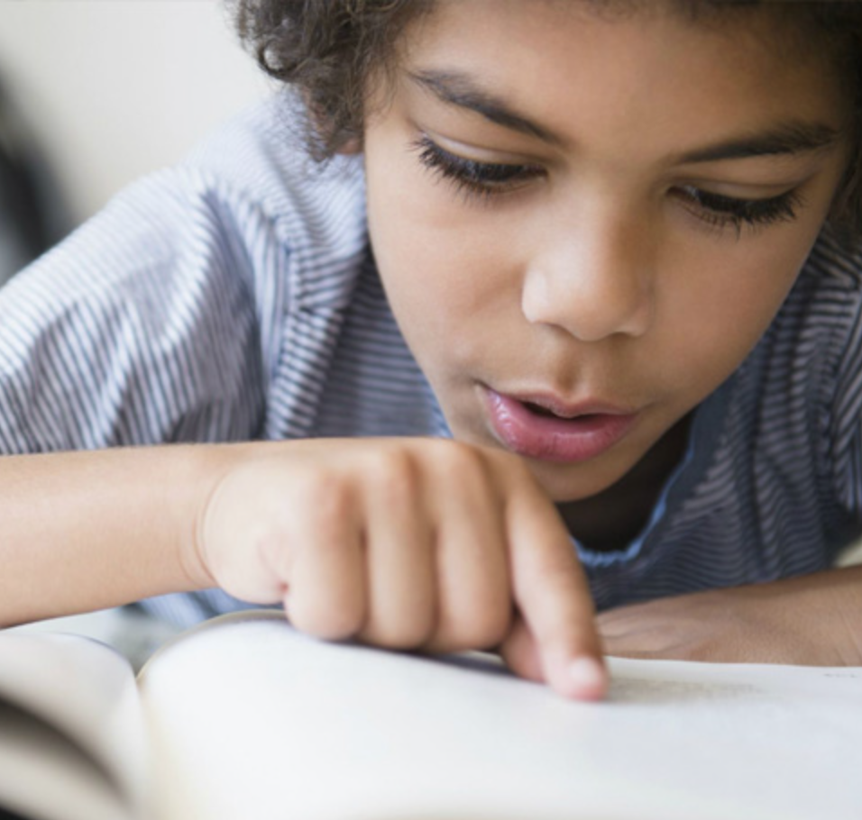 Student with curly hair reading a book during a dyslexia tutoring session