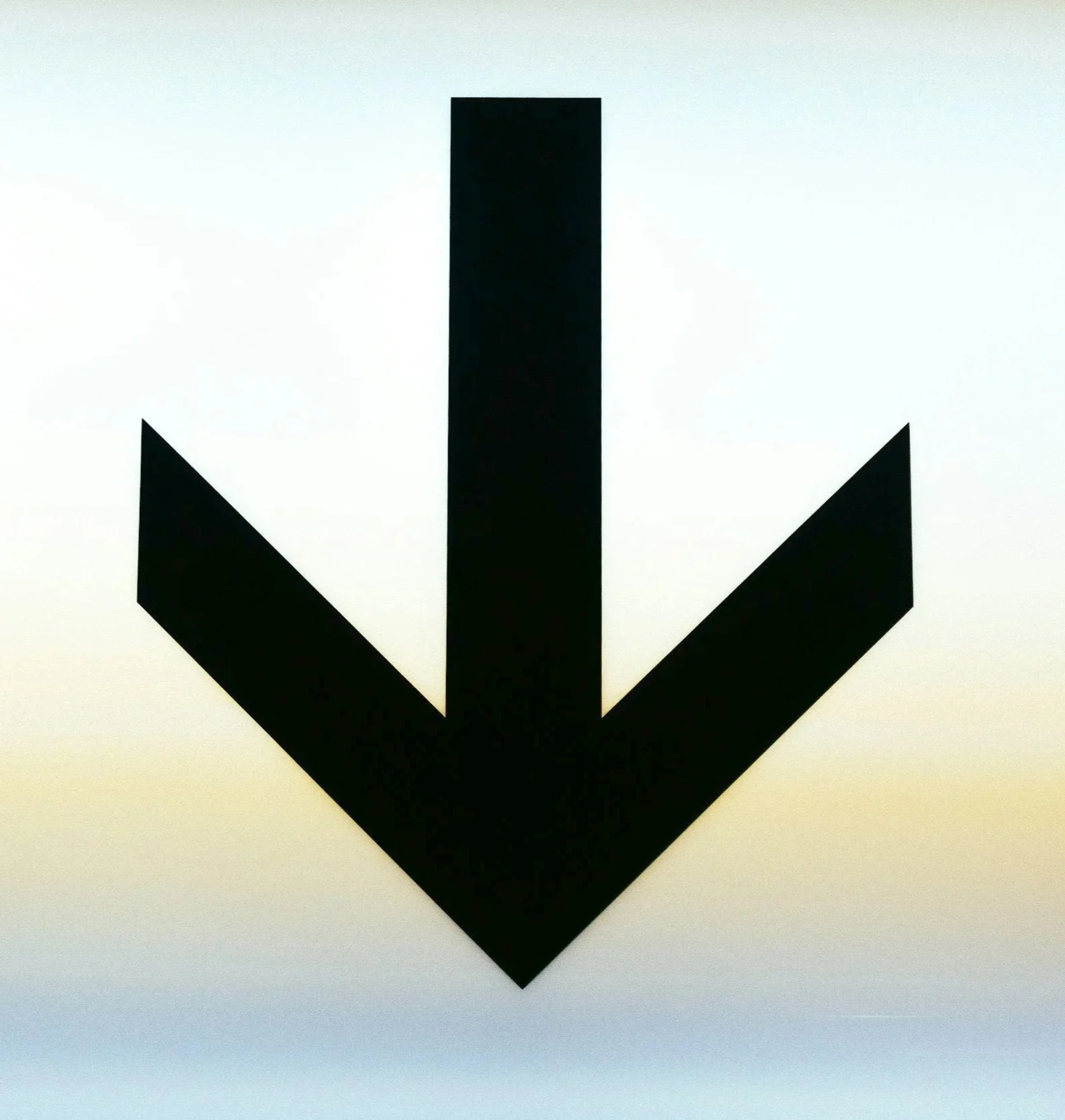 A black downward arrow sign with a vague background of a pastel-colored sky.