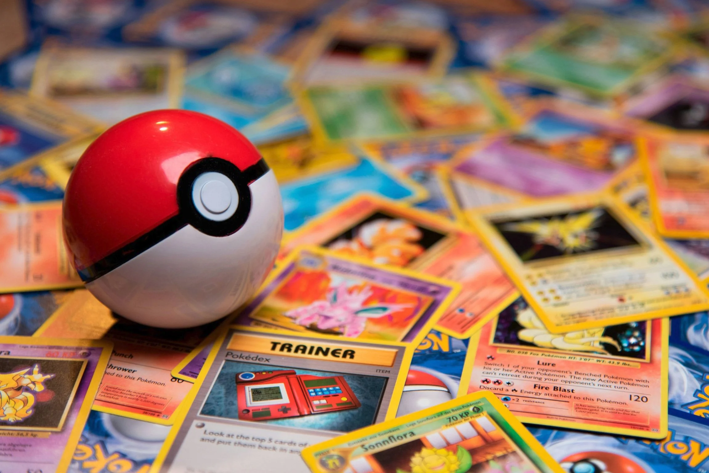 A Pokémon Poké Ball on top of a scattered assortment of Pokémon trading cards.