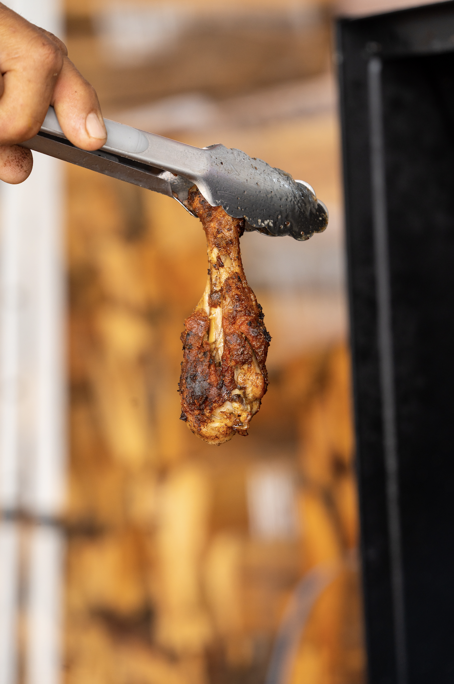 Person using tongs to pick up a cooked chicken drumstick from a grill or smoker.