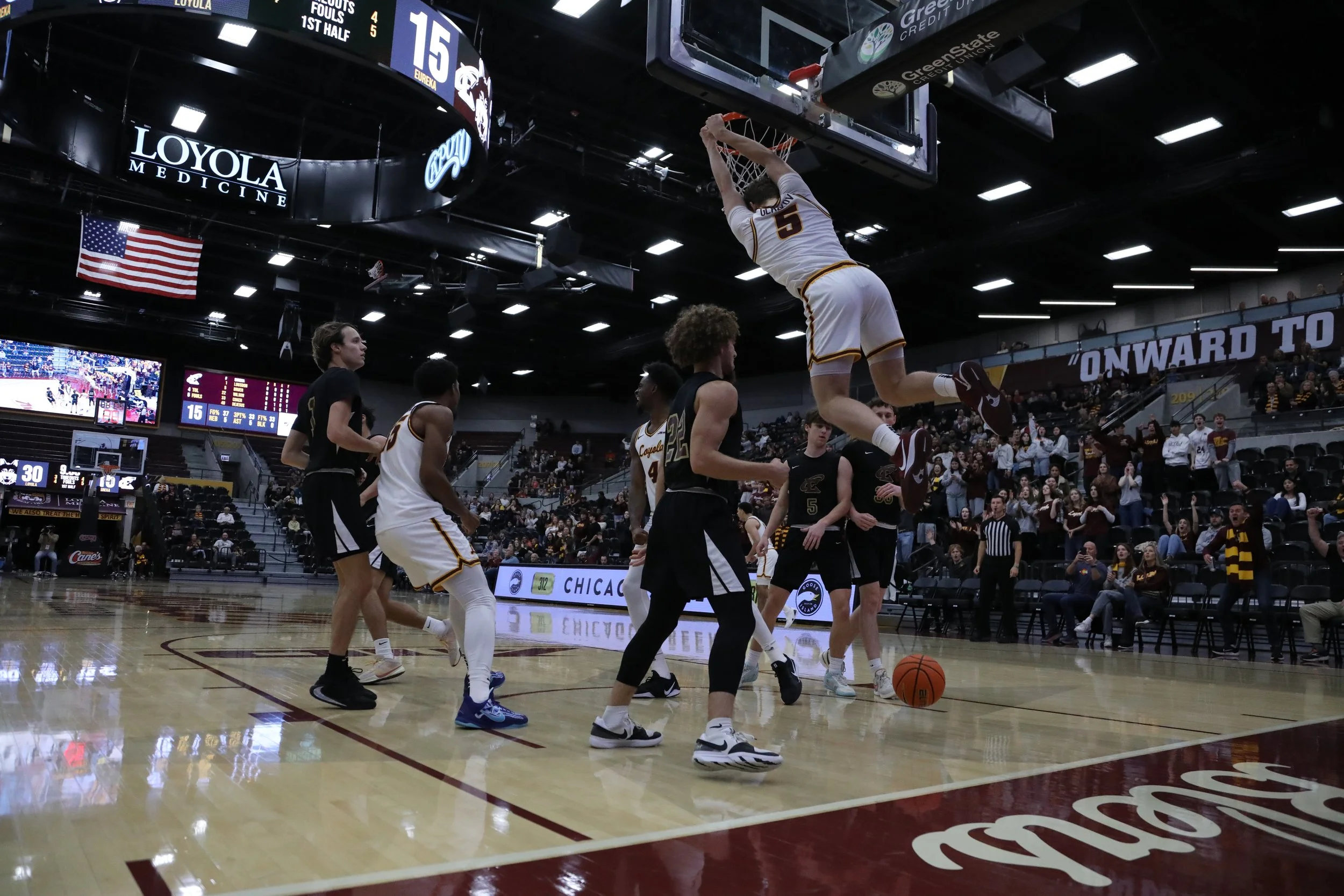 Basketball player dunking in a game with audience in the background in an indoor arena.