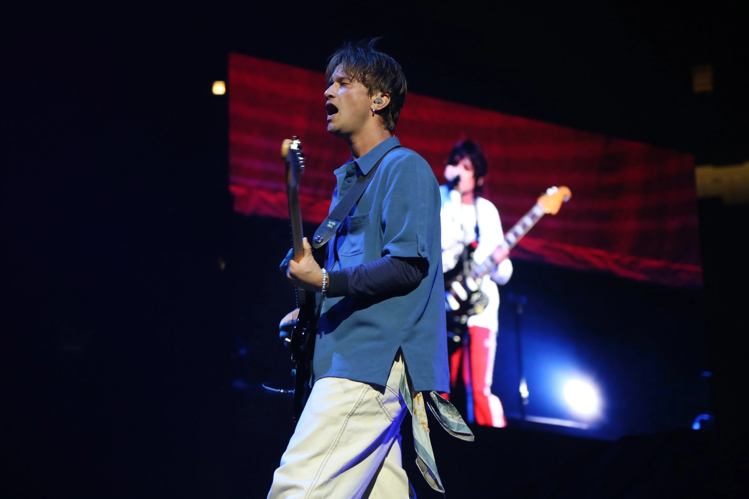 Musician playing guitar on stage with large screen in background
