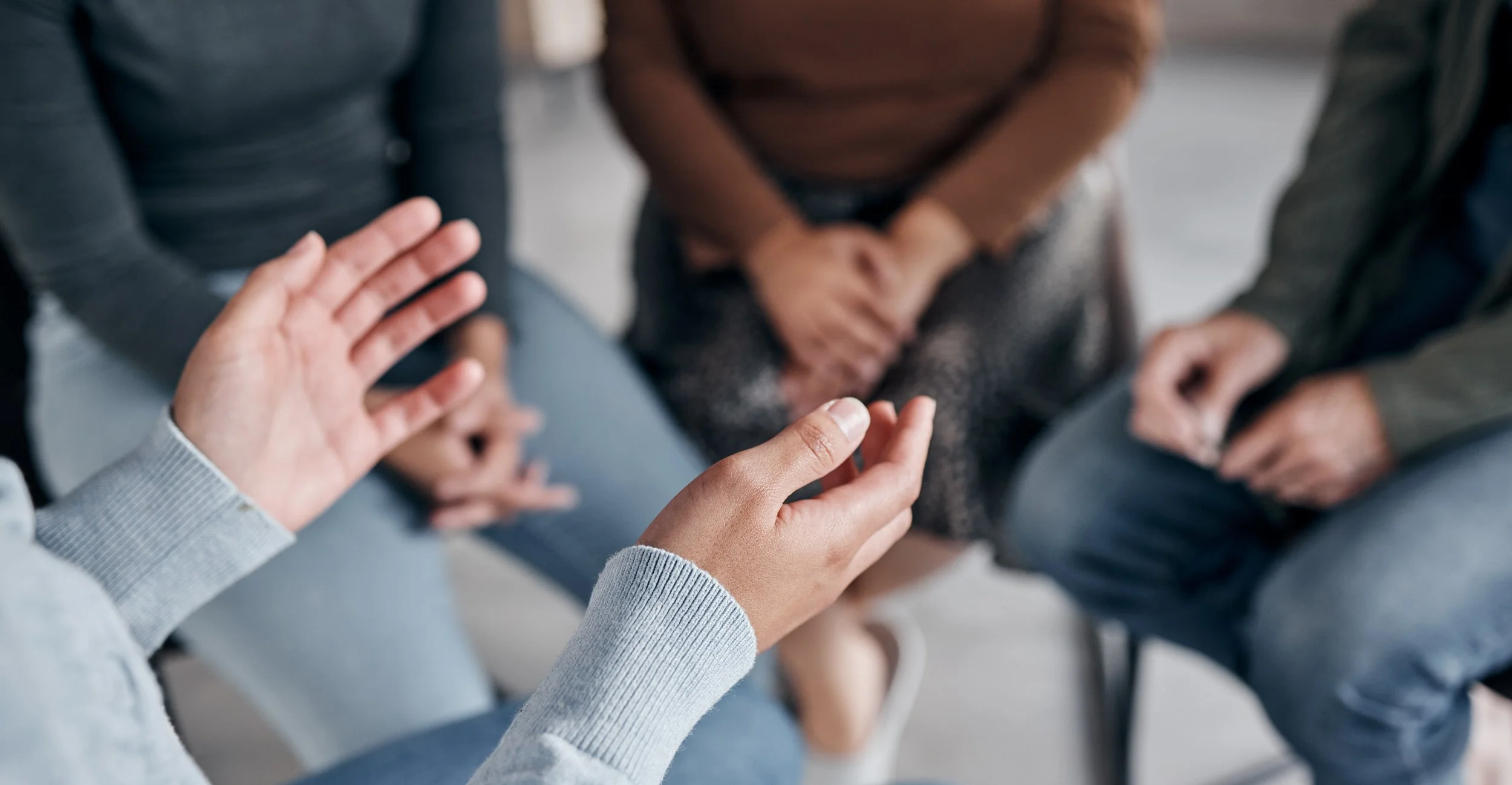 A group of people sitting in a circle, engaging in conversation with one person gesturing with their hand.