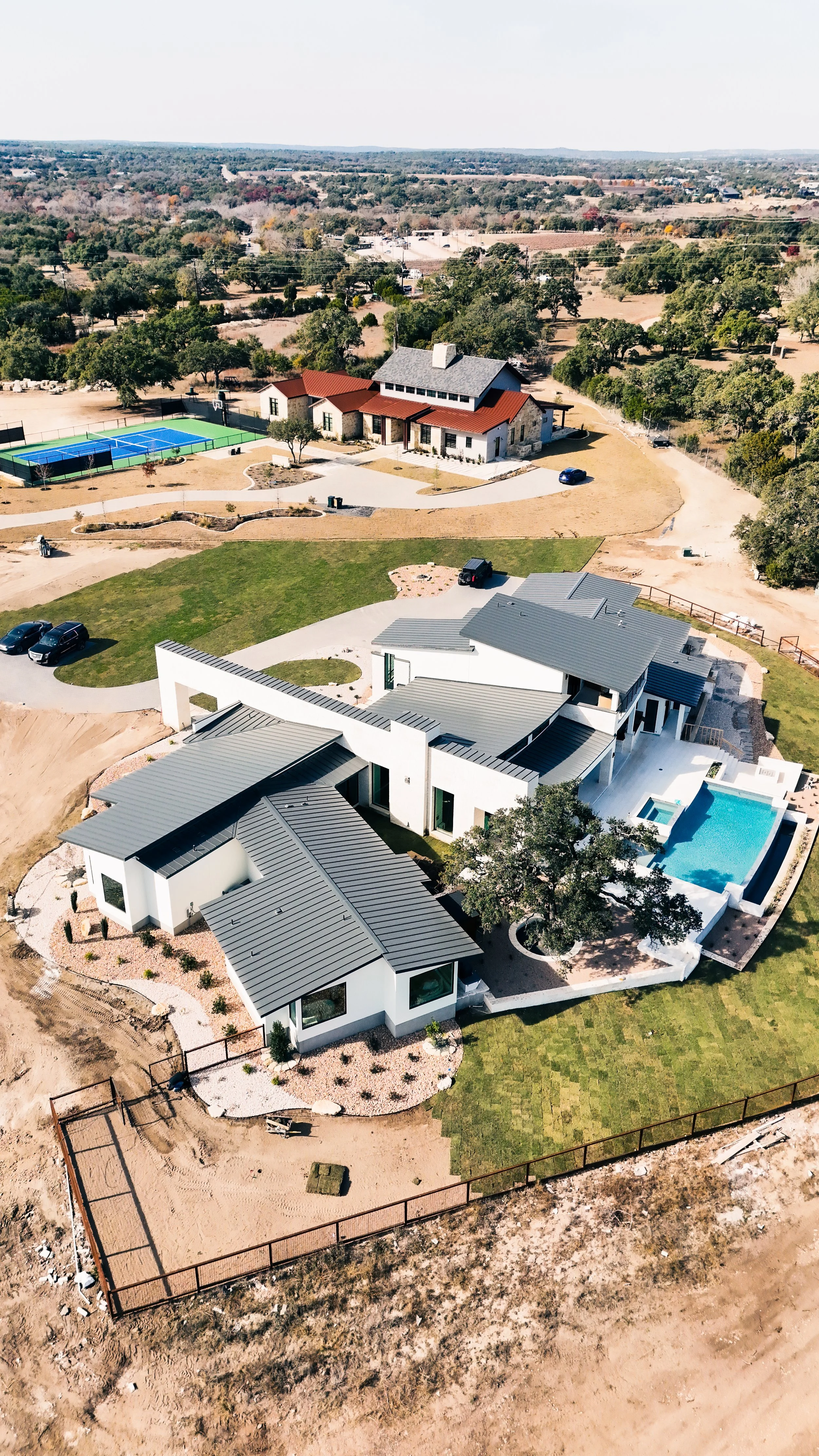 Aerial view of two modern houses with swimming pool and tennis court in a spacious suburban area.