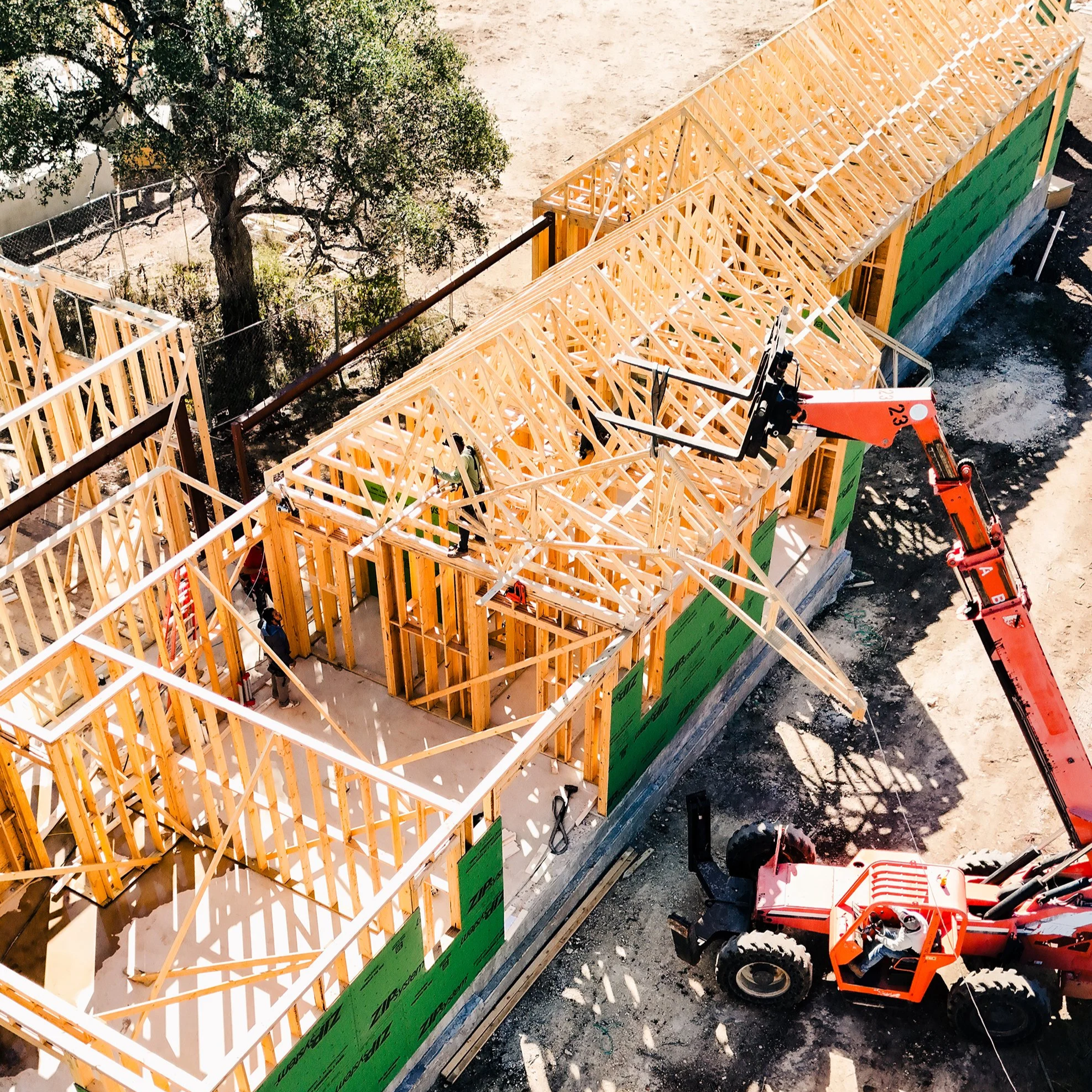 Construction site with wooden framing of a building, a tree, construction equipment, and a partially built structure.