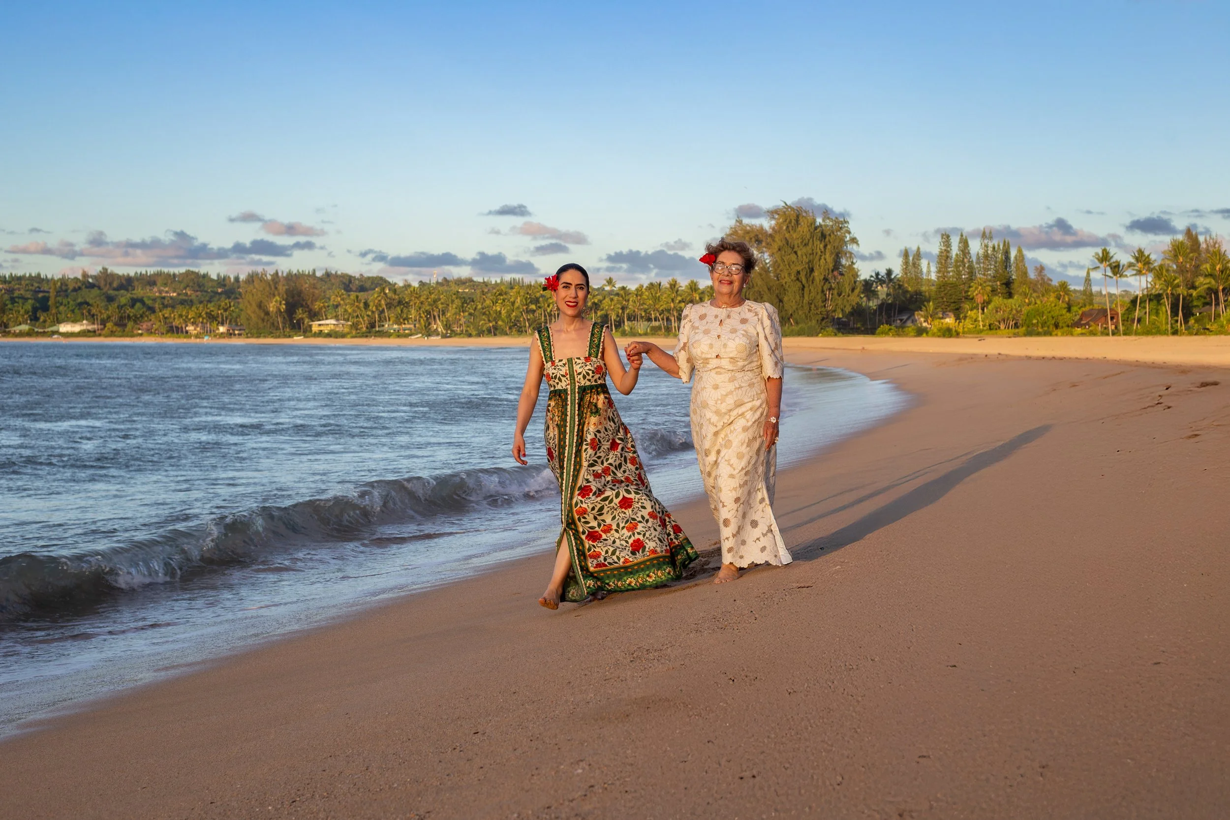 Two women holding hands walking on sandy beach with ocean waves in Cozumel