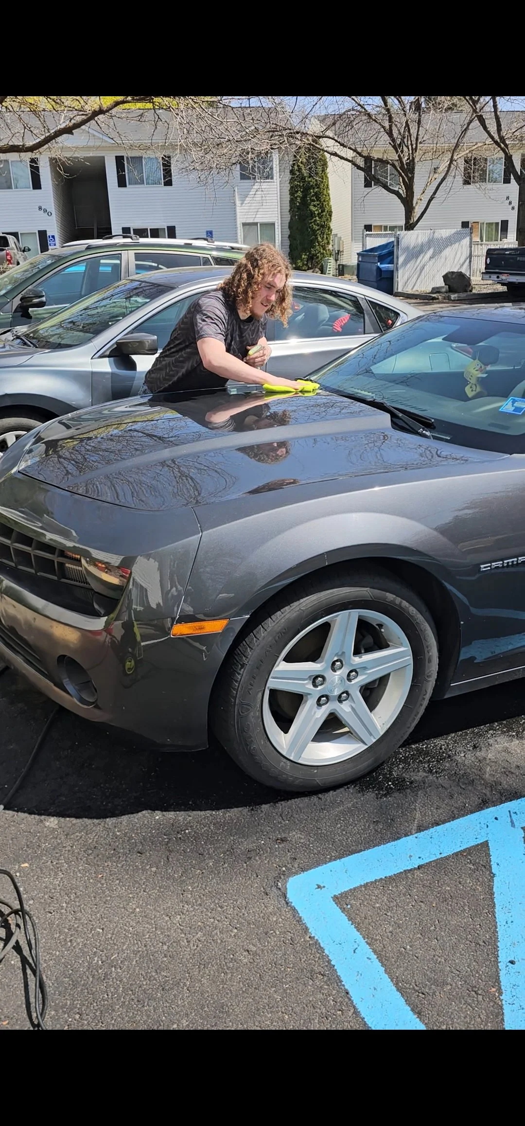 Tyler cleaning a gray Chevrolet Camaro in a parking lot.