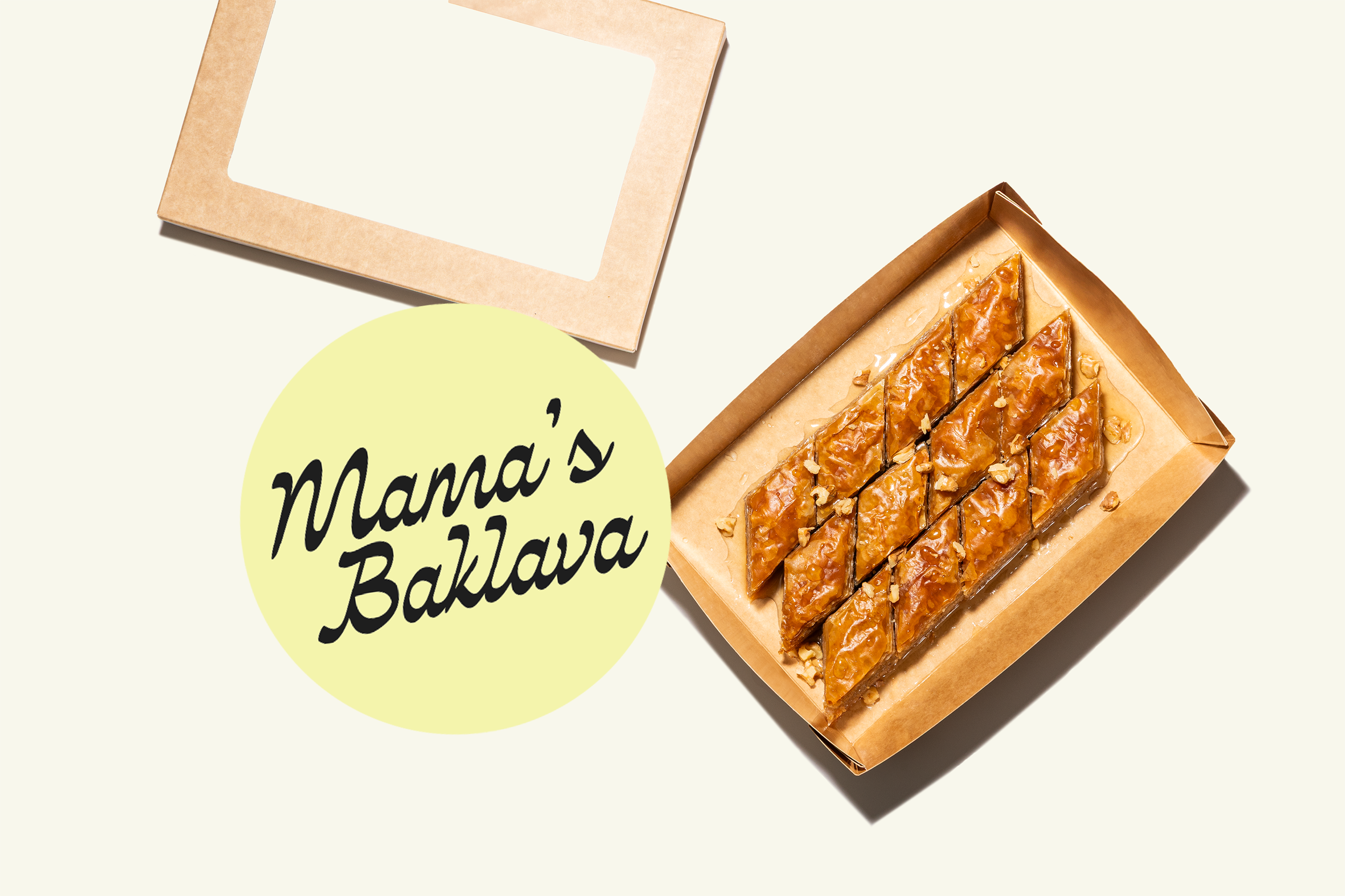 A brown cardboard tray with slices of baklava topped with chopped nuts on a light-colored background, with a round yellow label reading 'Mama's Baklava' and a beige box with a window near the top of the image.