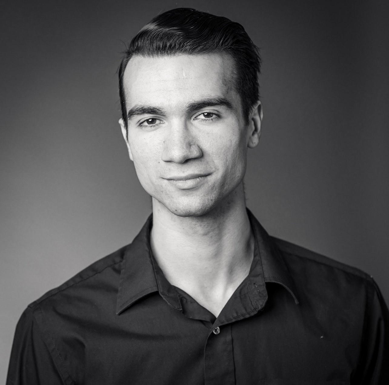 Black and white portrait of a young man with dark hair, wearing a collared shirt, looking directly at the camera with a slight smile.