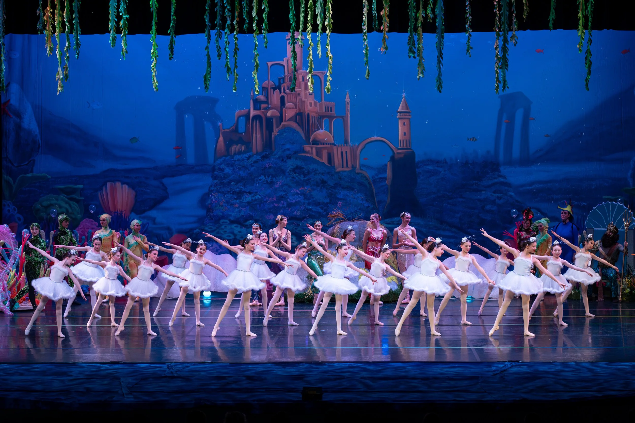 Ballet dancers perform on stage with a colorful underwater scene backdrop, featuring a castle and aquatic elements.