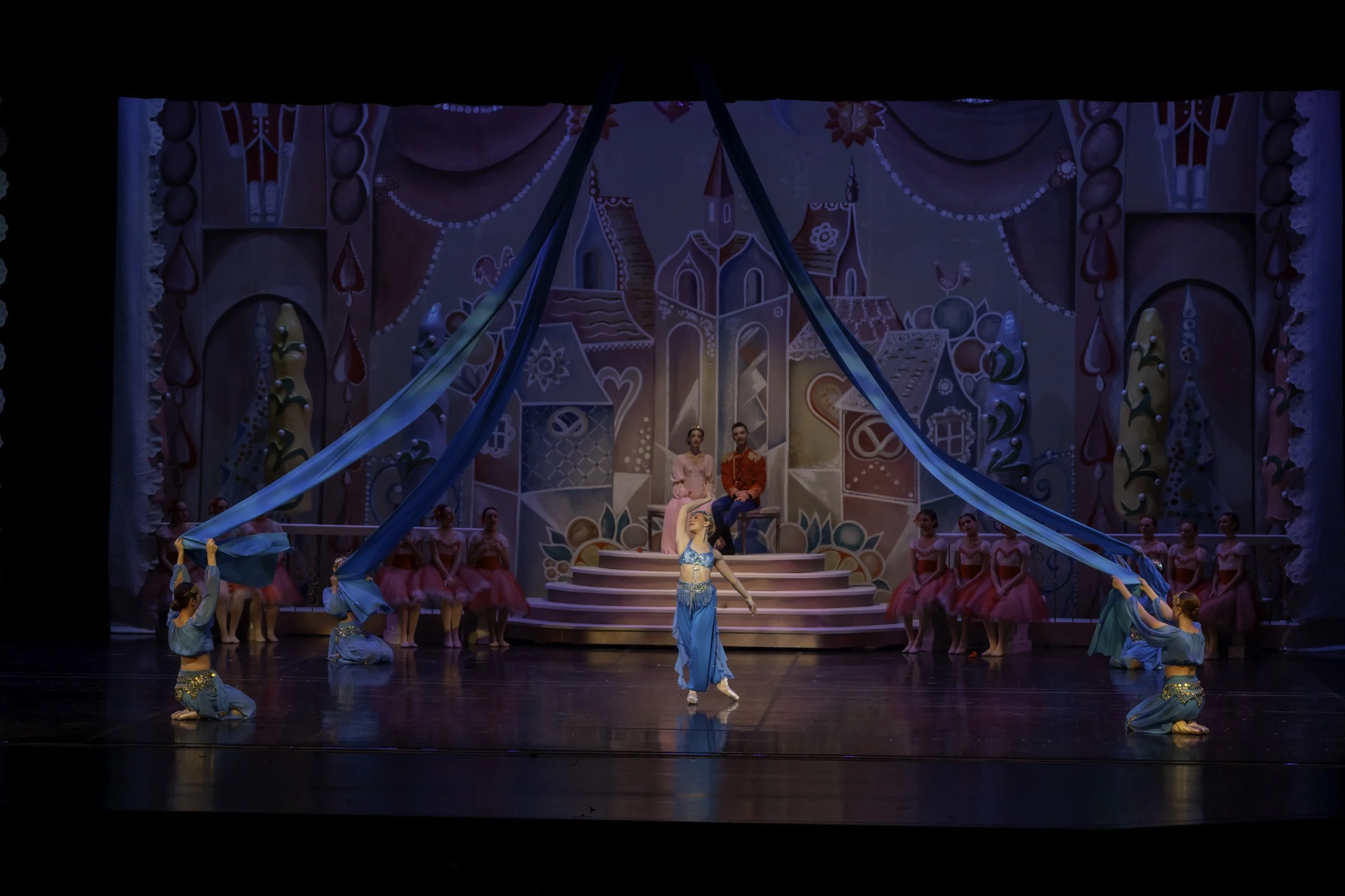 A ballet performance on stage featuring dancers in colorful costumes with a whimsical, fairy-tale backdrop.