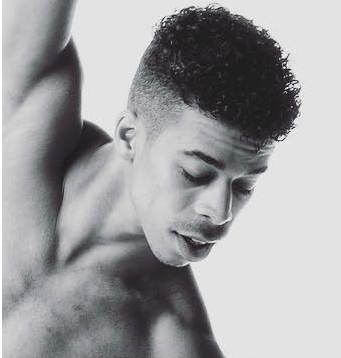 Close-up black and white photo of a shirtless young man with curly hair, looking downward.