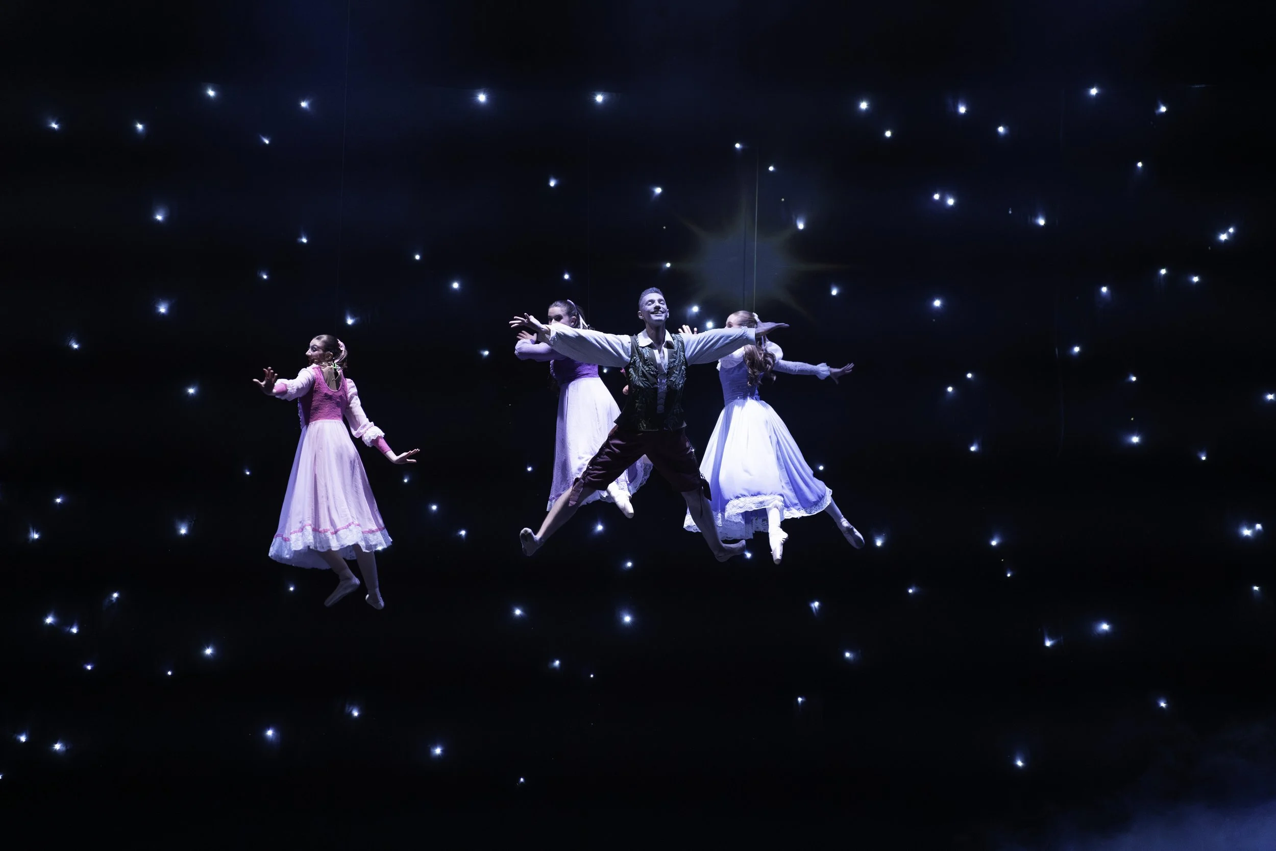 Four ballet dancers performing on stage with a starry background and blue lighting.
