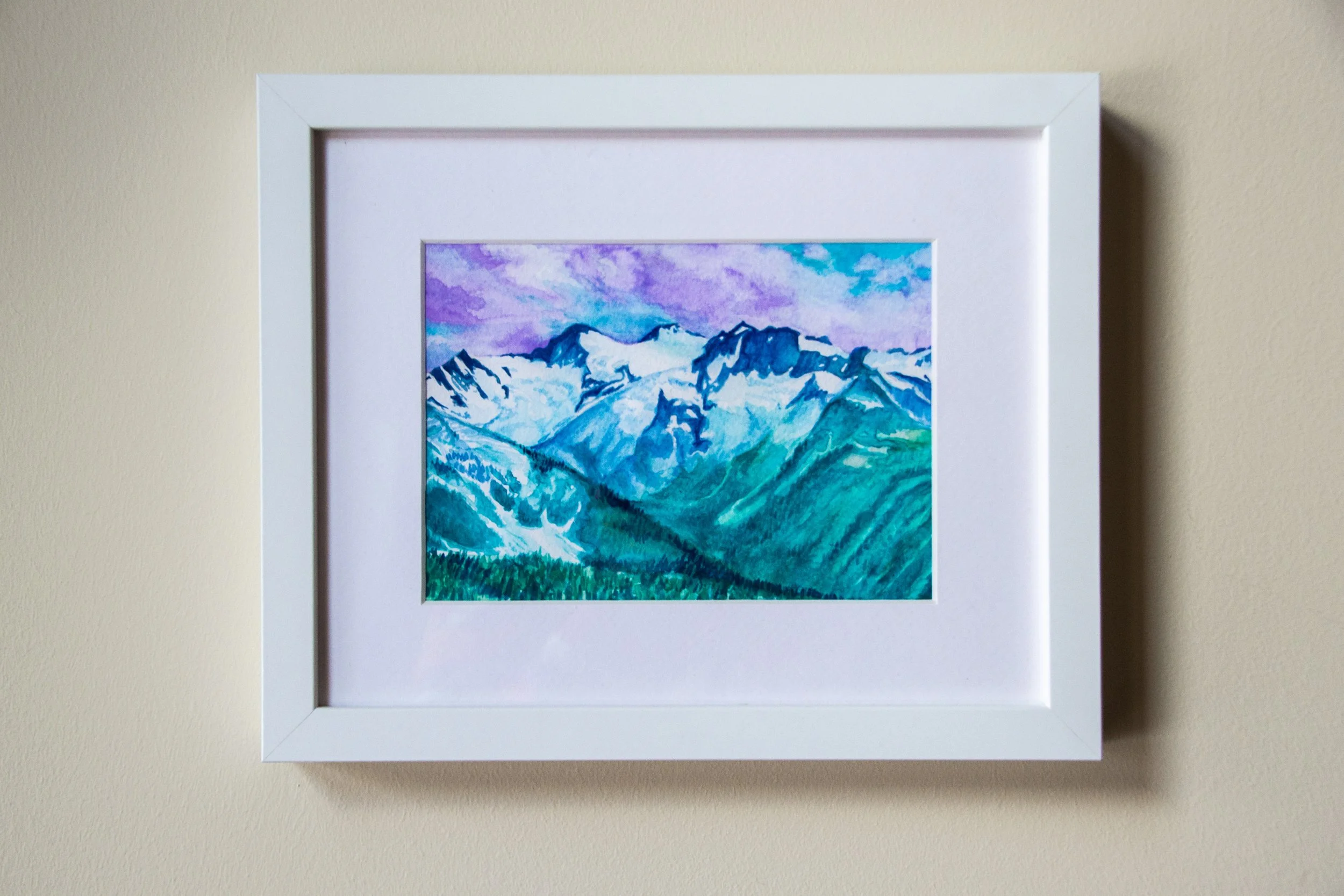 Framed watercolor painting of snowy mountains under a colorful sky.