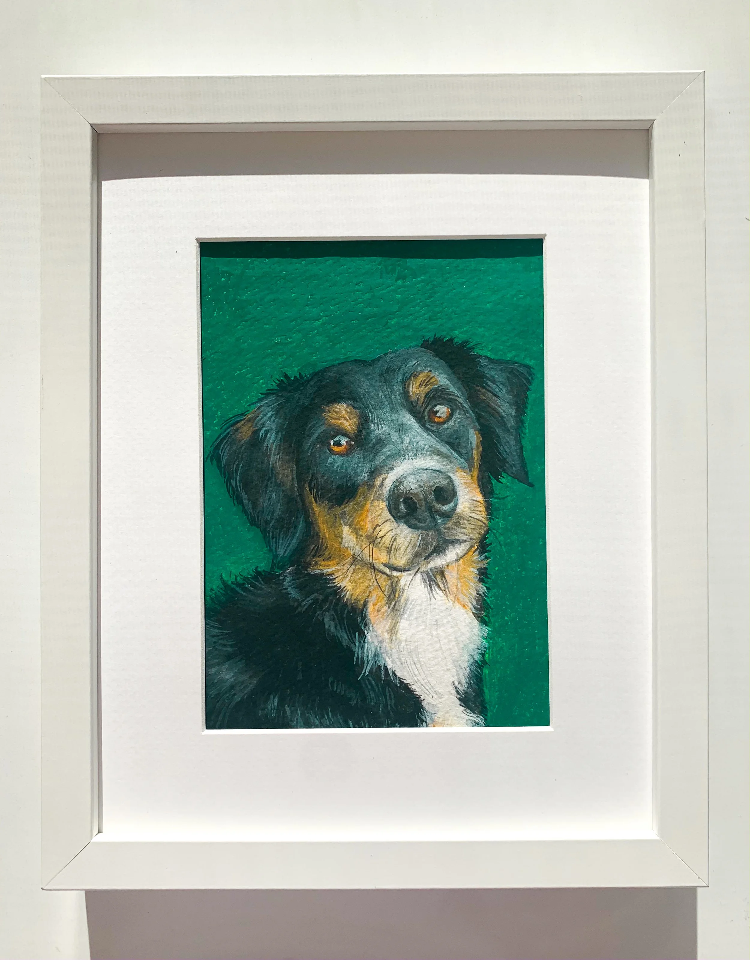 Framed artwork of a dog with a black, brown, and white coat against a green background.
