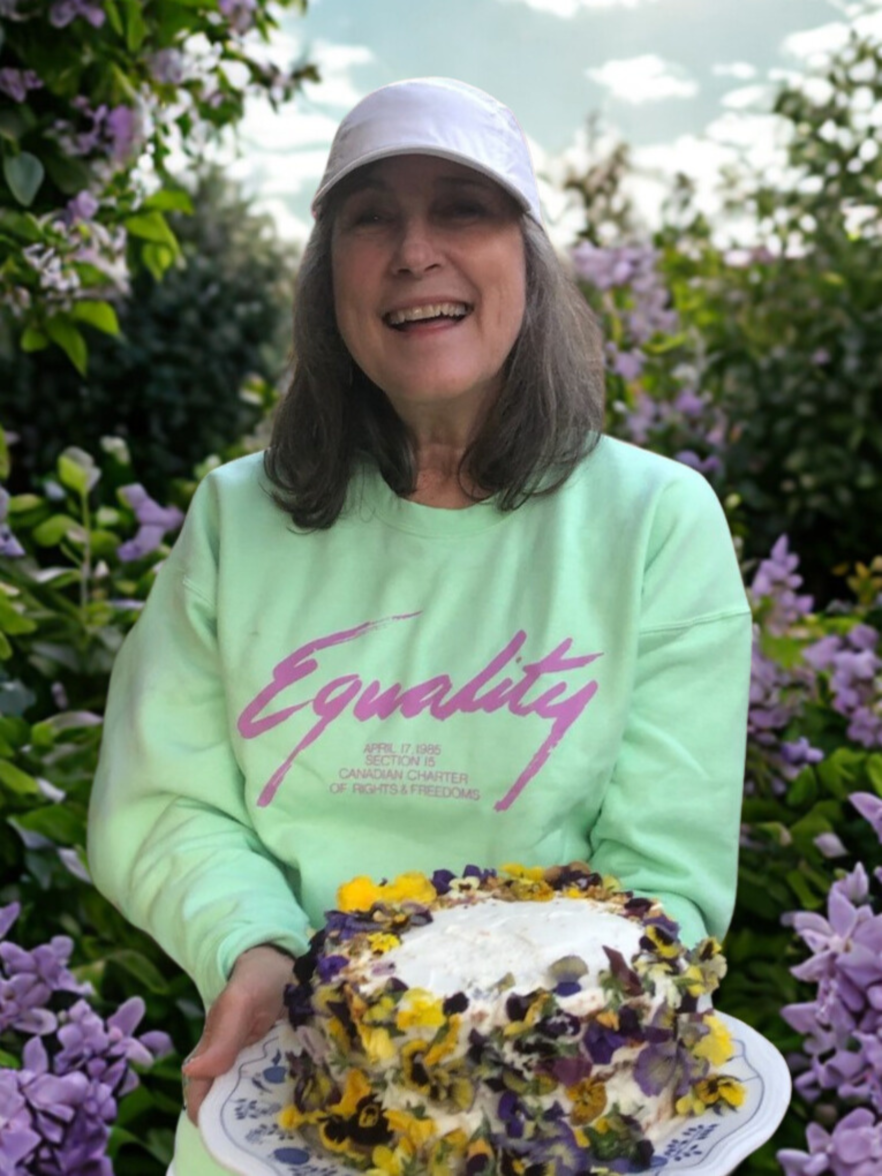 A woman smiling, holding a cake decorated in flowers.