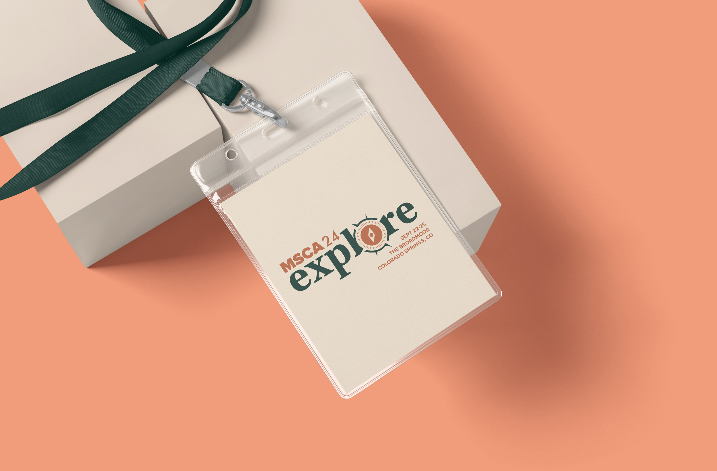 Event badge with logo and event details on a lanyard, placed on a white box with a peach-colored background.
