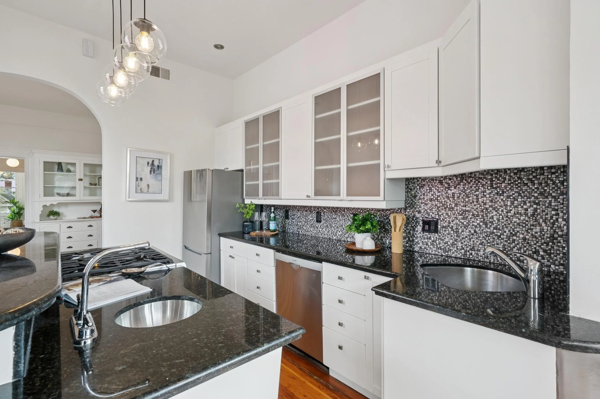 Modern kitchen with white cabinets, black granite countertops, mosaic tile backsplash, stainless steel appliances, and a small sink on the countertop.