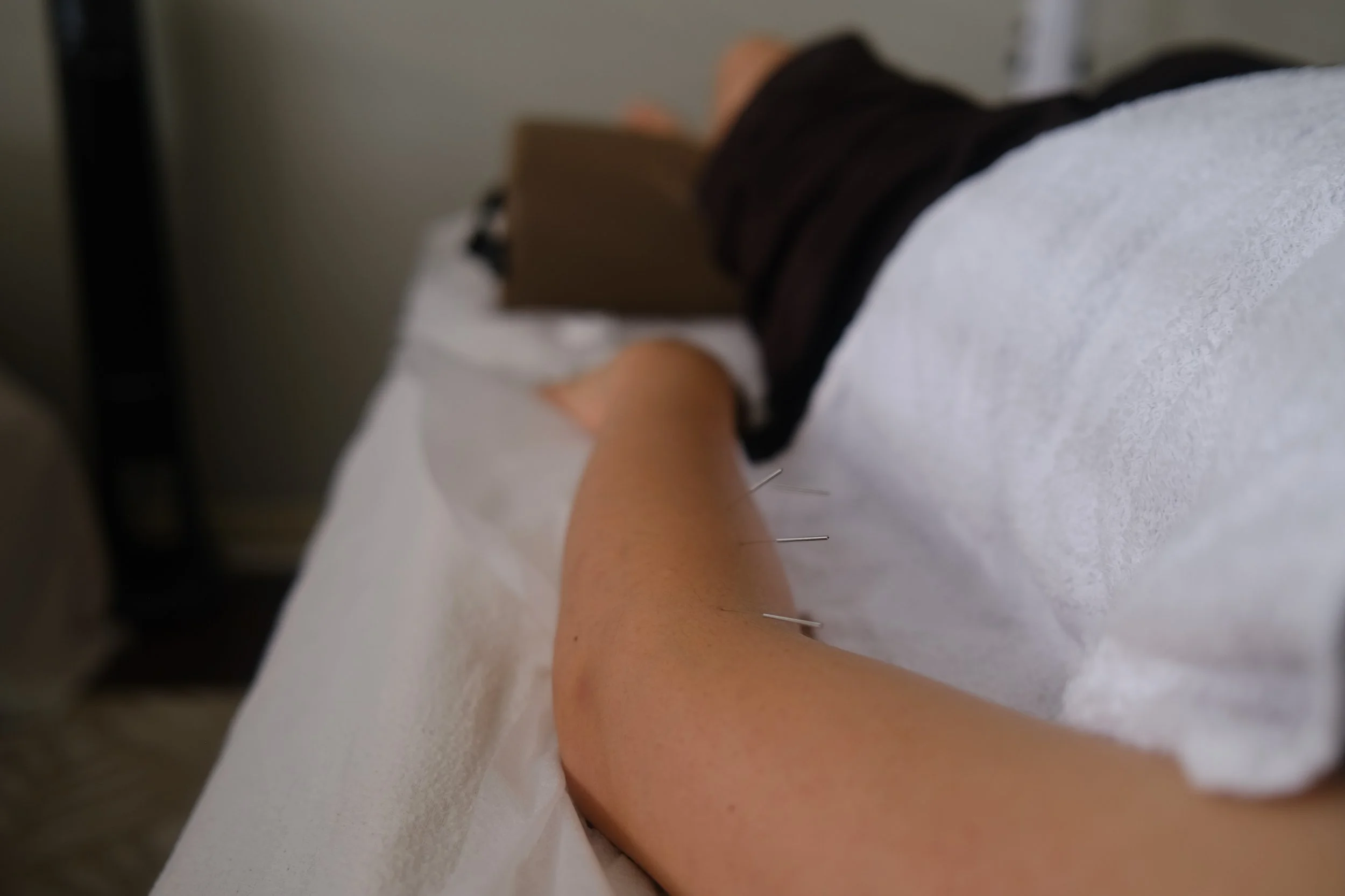 A pair of hands holding three gua-sha stones of green, pink, and white color with marbled patterns.