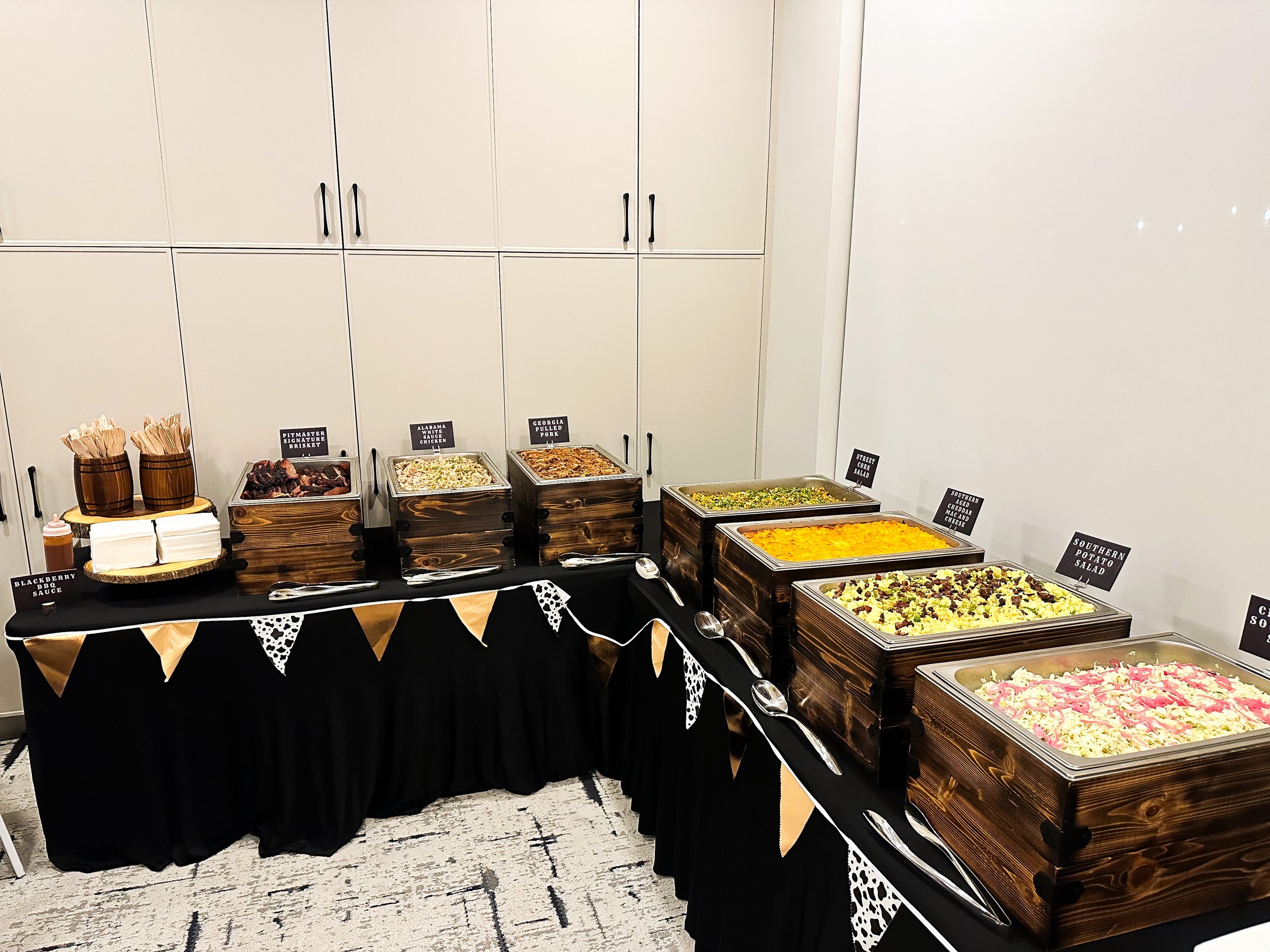 Buffet table with various dishes in wooden chafing dishes and containers, including potato salad, a casserole, and meat, with serving utensils and napkins. a Great Catering event for our friends at Weibe Properties in Abbotsford BC
