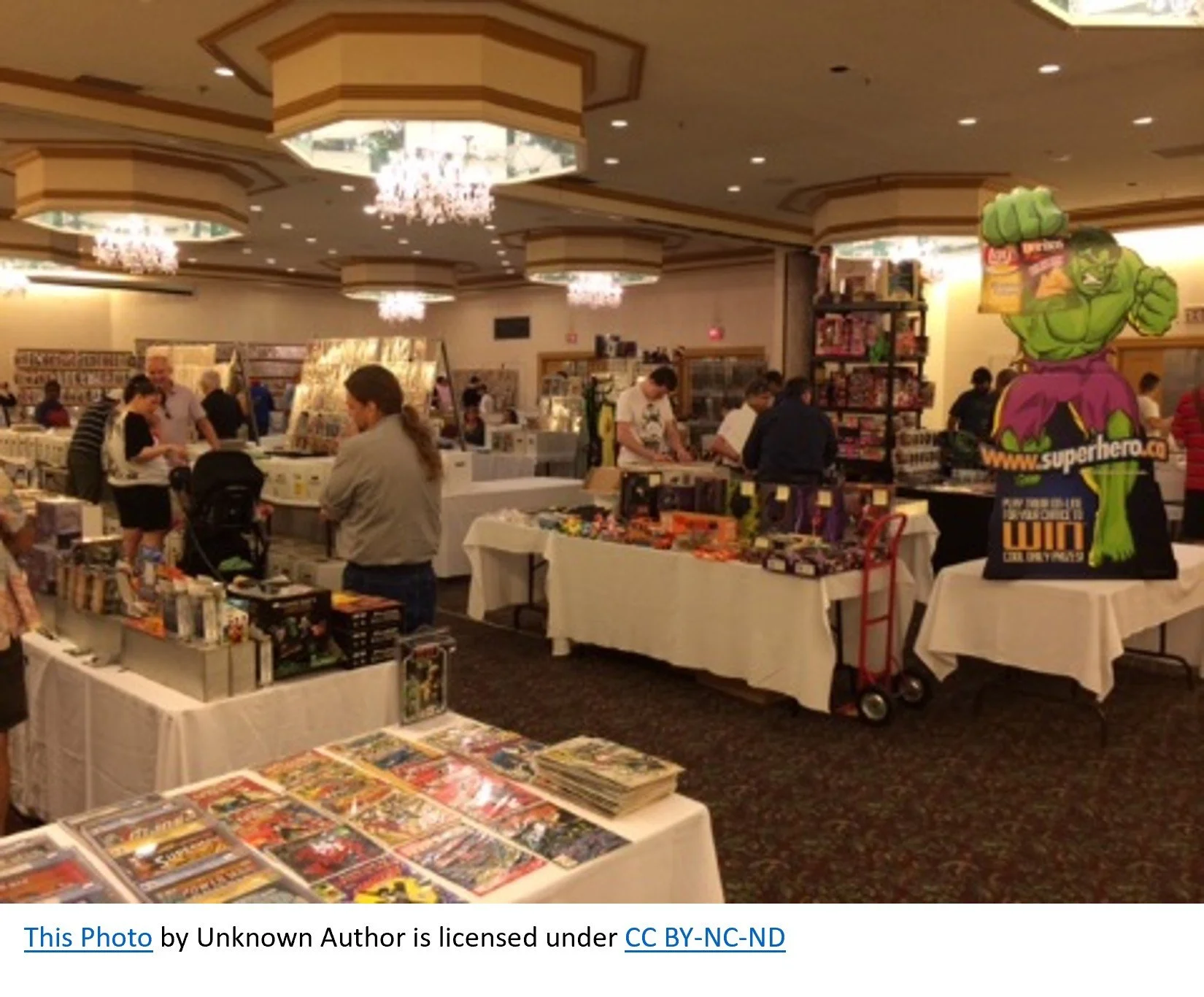 People browsing tables with comic books and collectibles at an indoor convention or store.